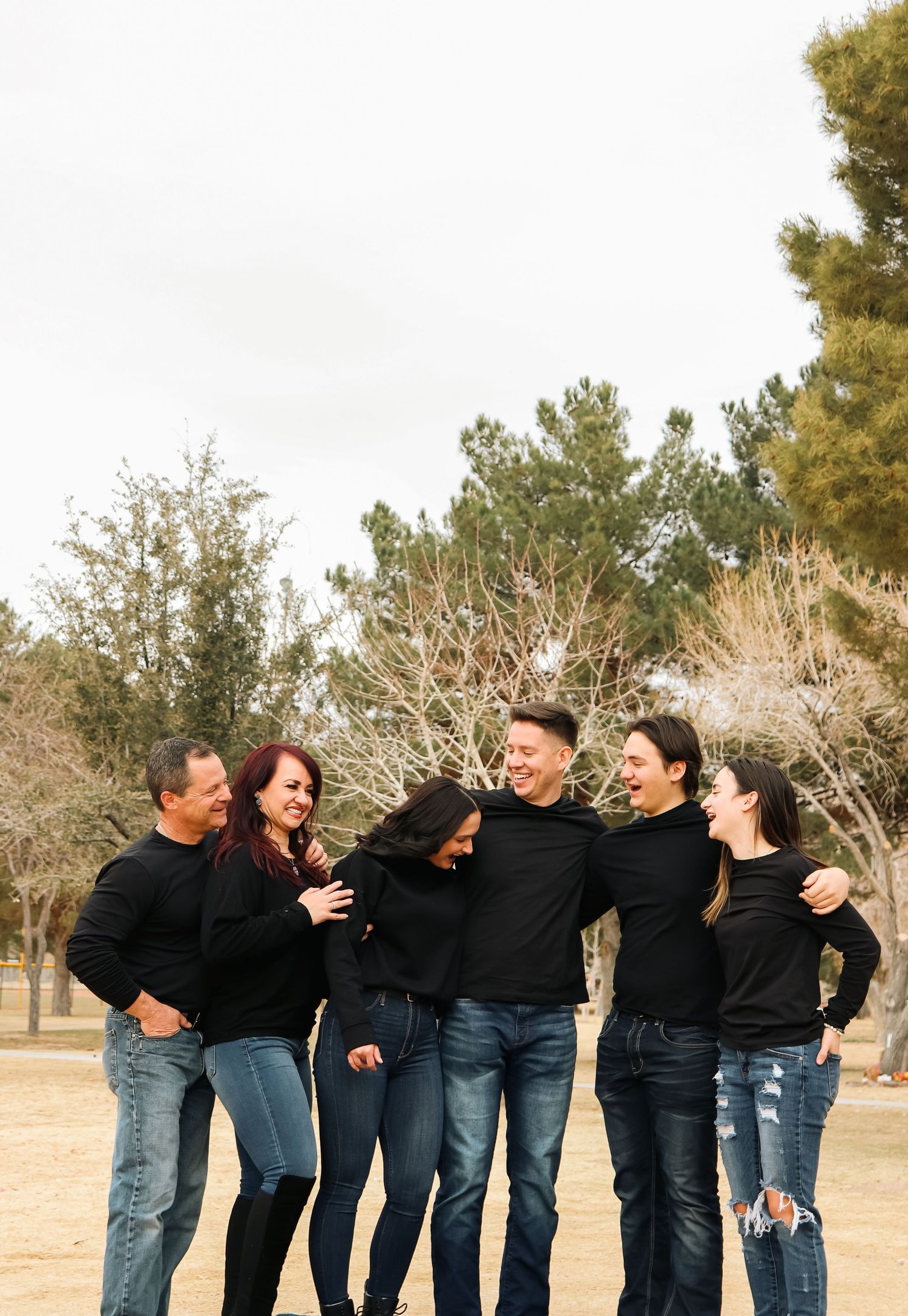 Six friends in matching black outfits laugh together during an outdoor photo session.