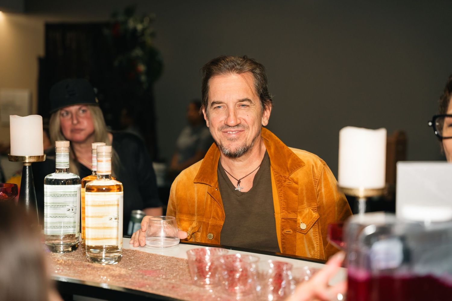 A person enjoys drinks at a dimly lit bar counter with bottles and glassware visible.