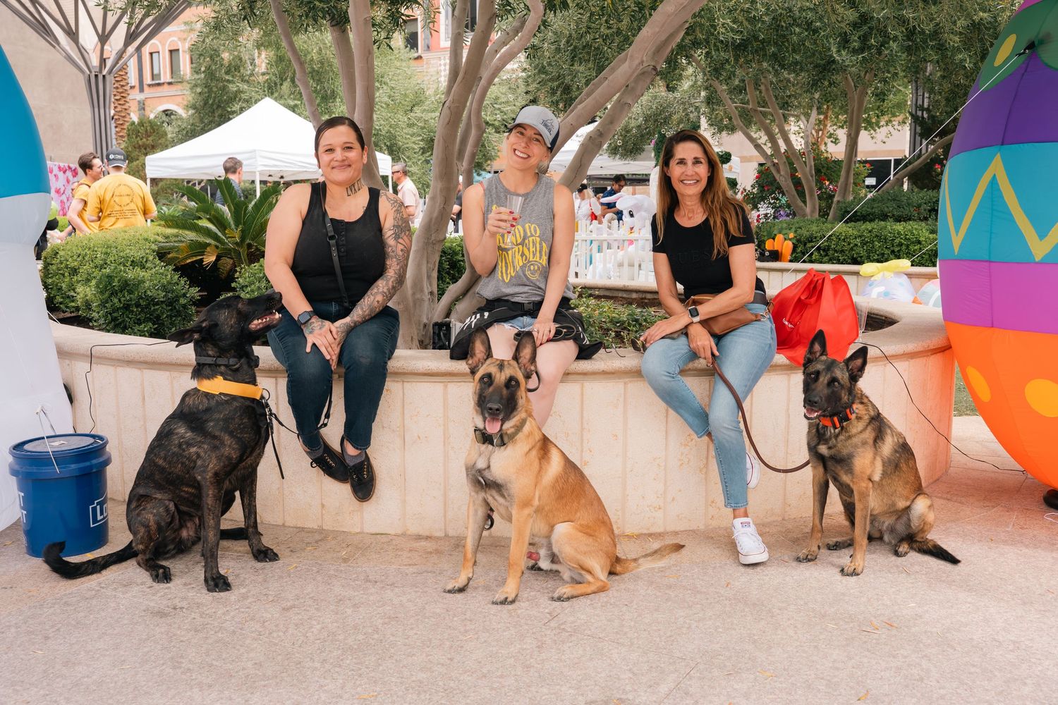 Group of people sitting on bench with their dogs at outdoor community event.
