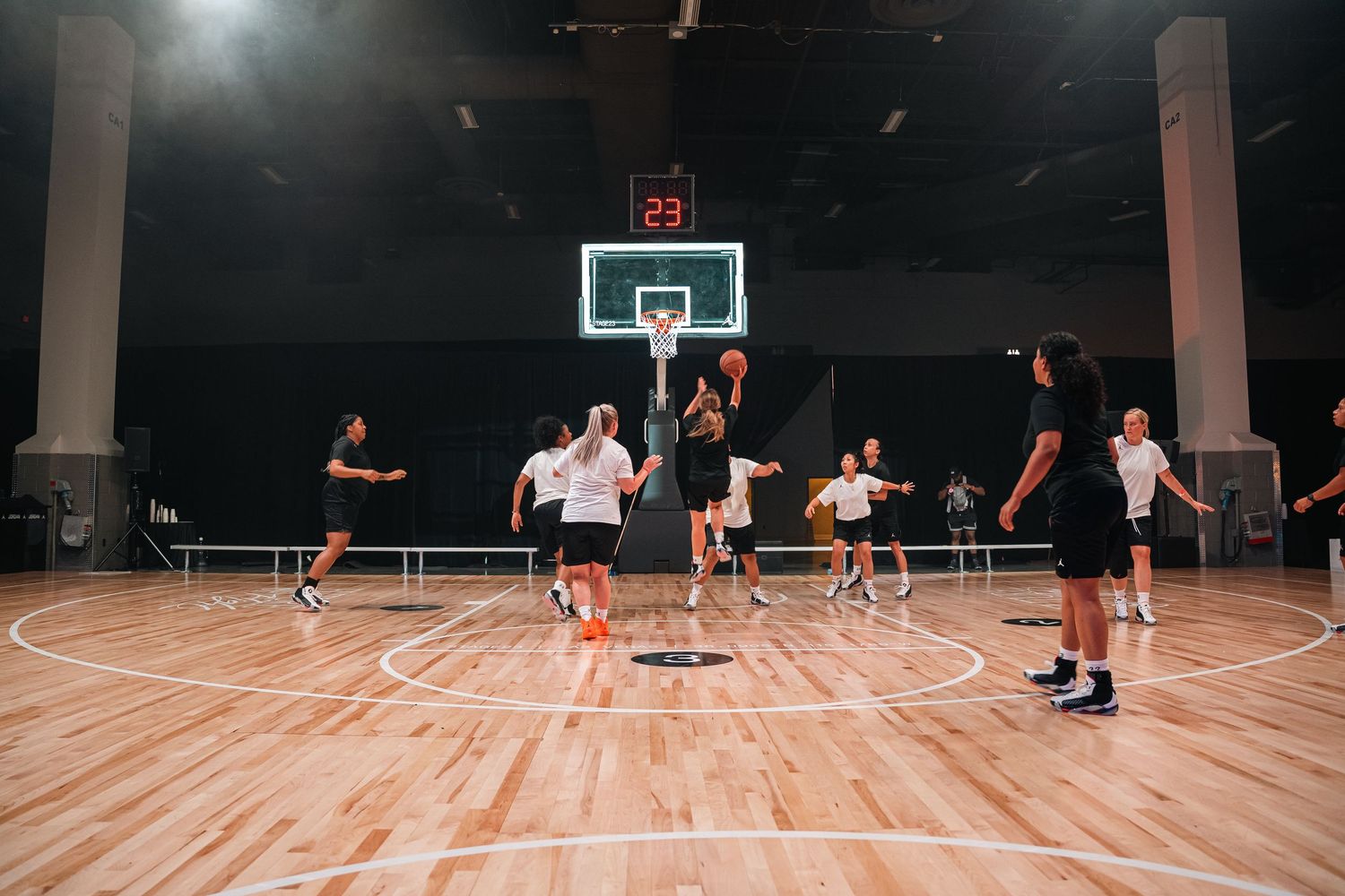Players engaged in a basketball game on wooden court under bright indoor lighting.