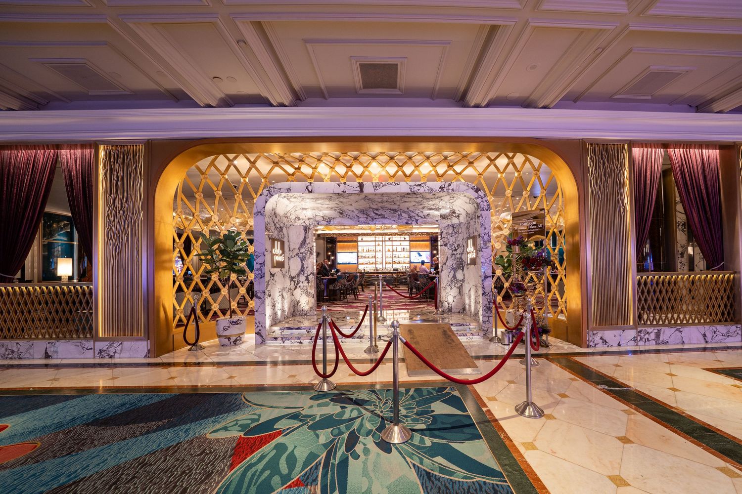Elegant cruise ship entrance with lattice-patterned walls, marble columns, and velvet ropes leading to a grand foyer.