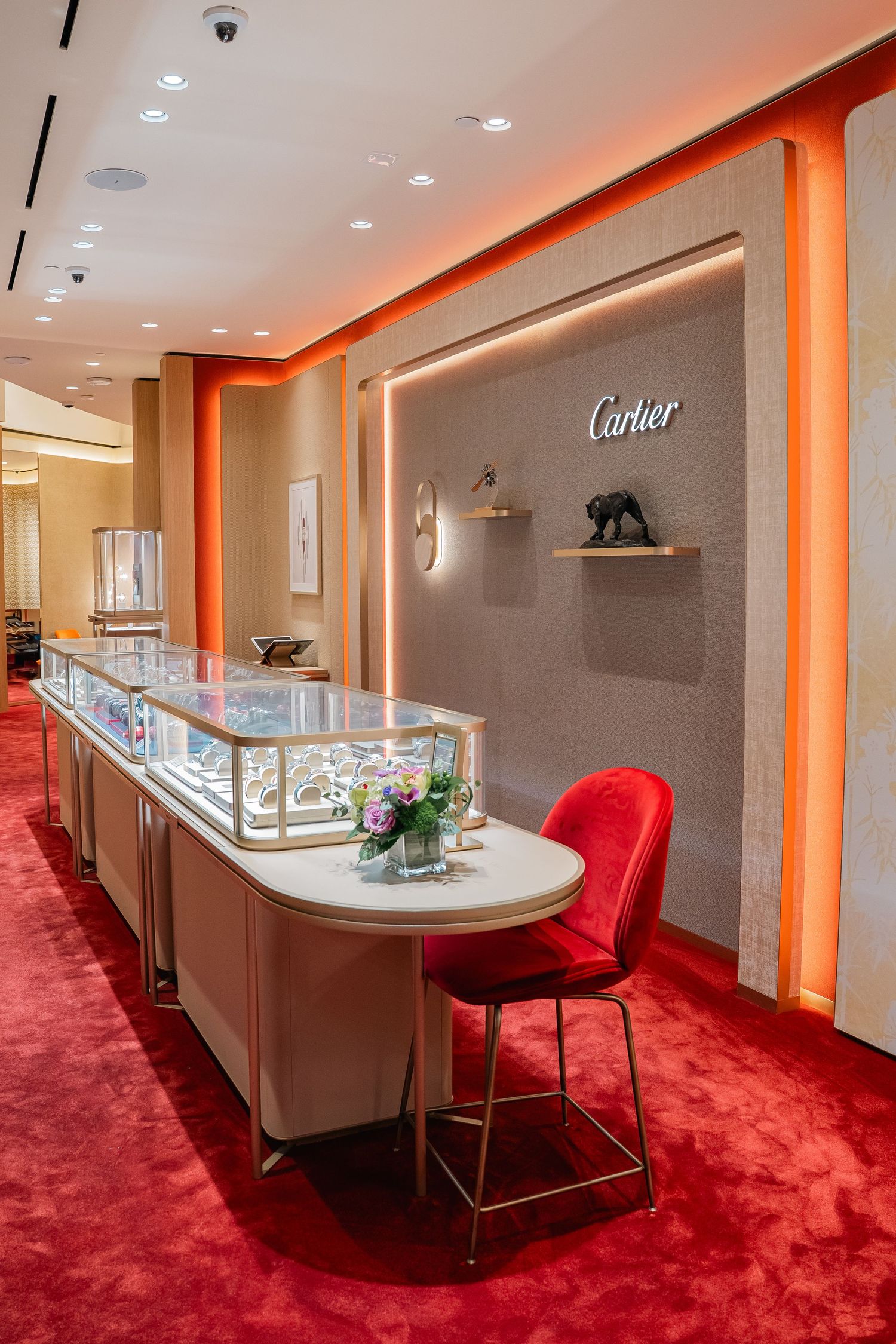 Cartier boutique featuring red carpeting, white display cases, and elegant lighting design.