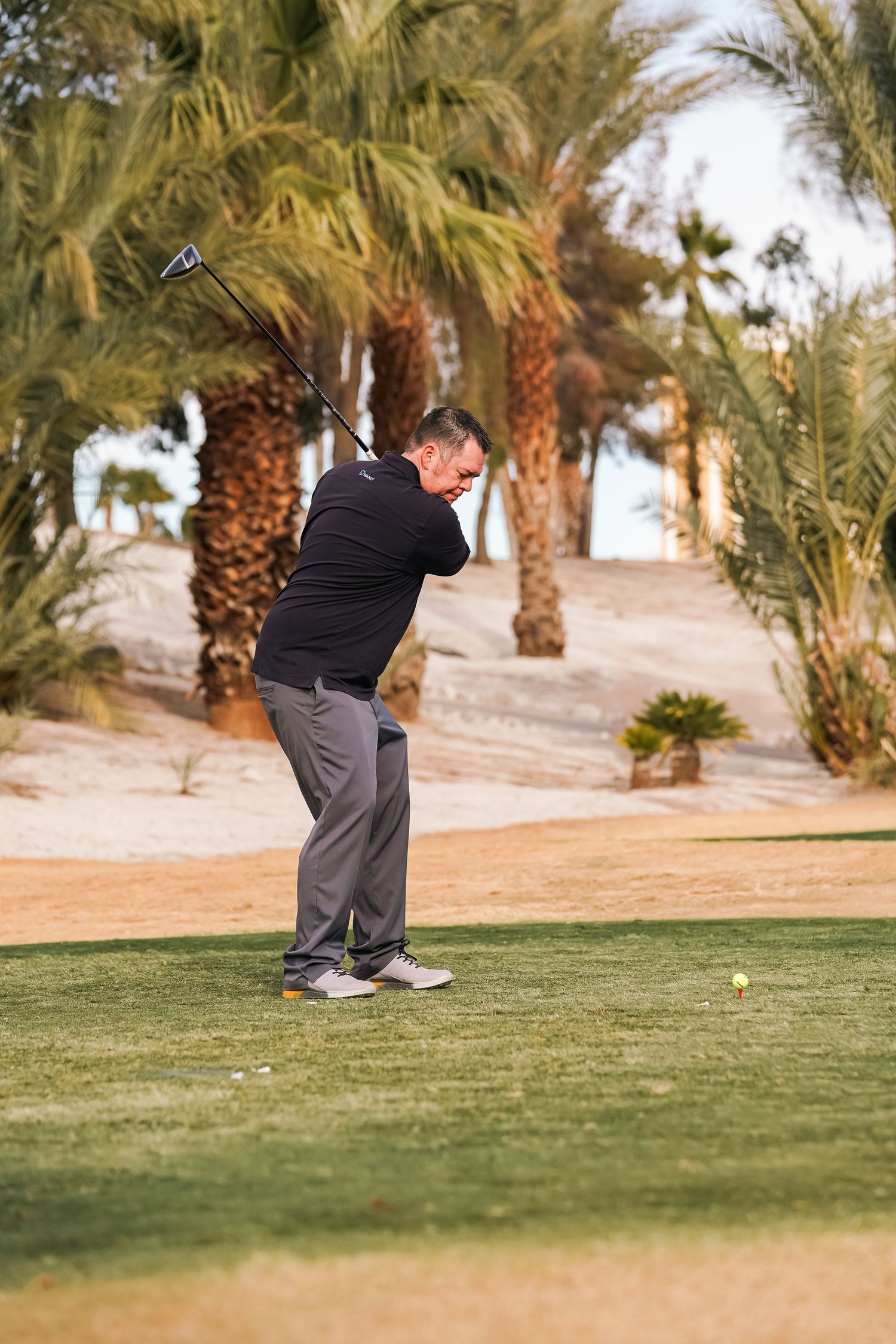 Golfer following through on swing against backdrop of desert palm trees.