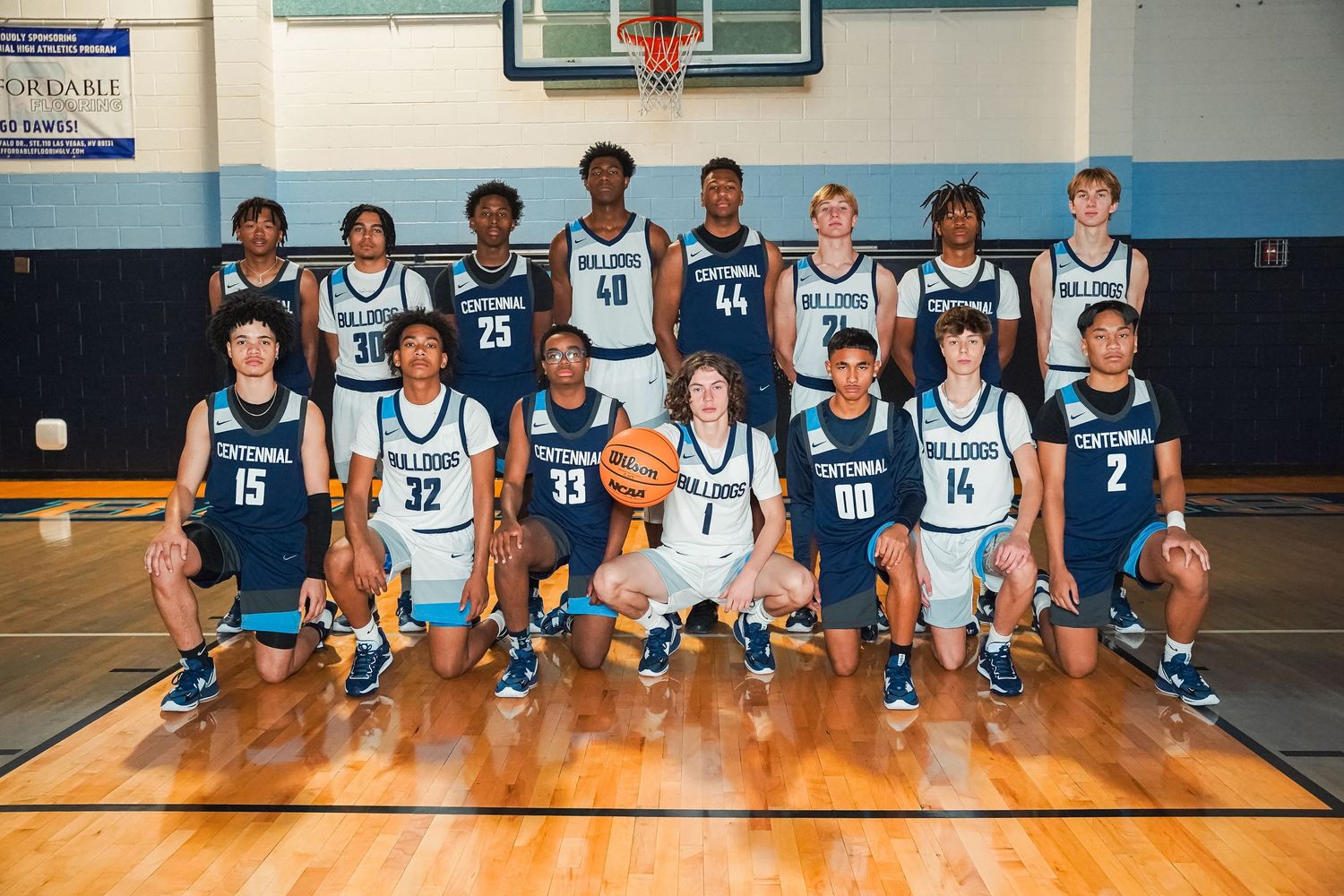 Team photo of basketball players in blue and white Bulldogs uniforms on court.