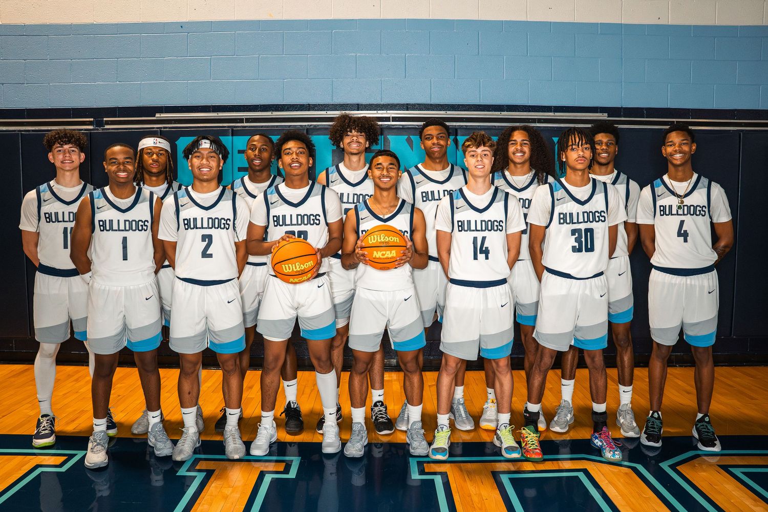 High school basketball team posed together in white uniforms on court.