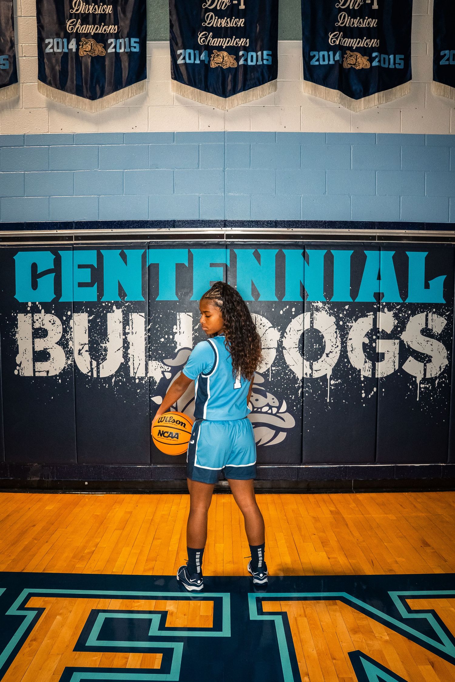 Basketball player practicing dribbling drills in front of Centennial Bulldogs wall mural.