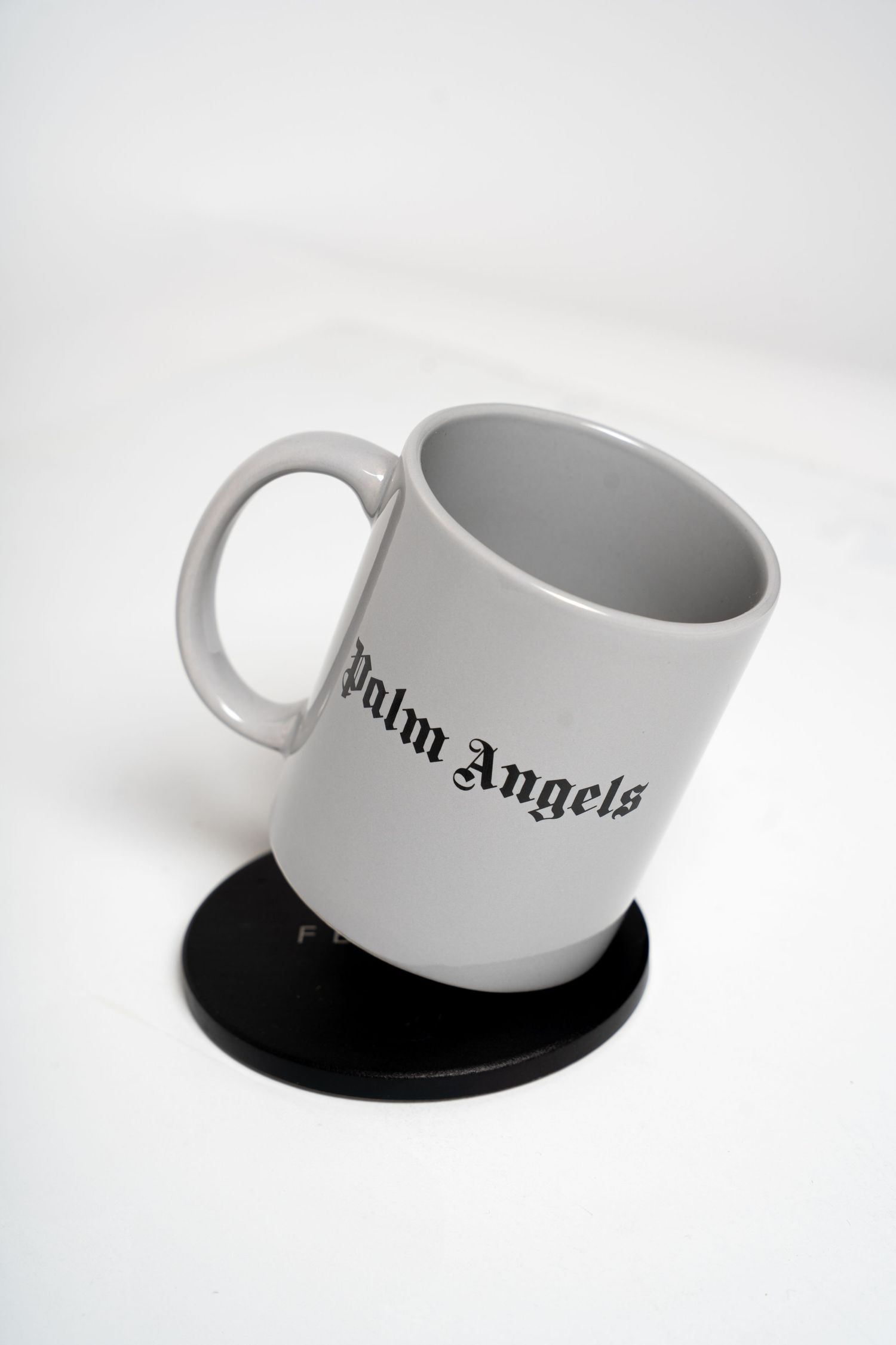 White ceramic mug with Palm Angels branding on black coaster against white background.