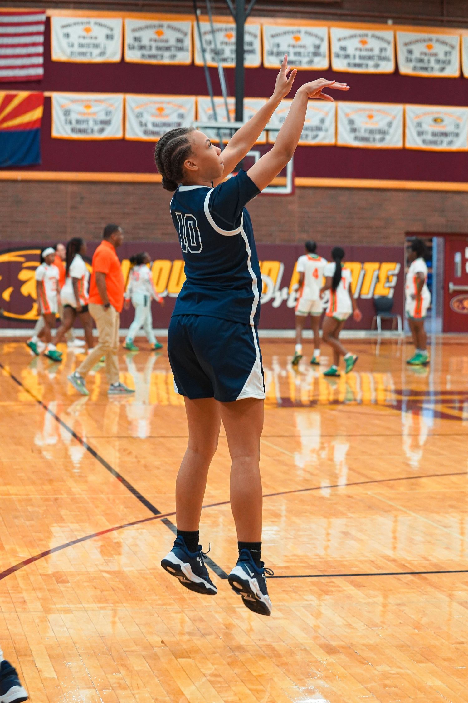 Players practicing jump shots on basketball court with championship banners visible in background.