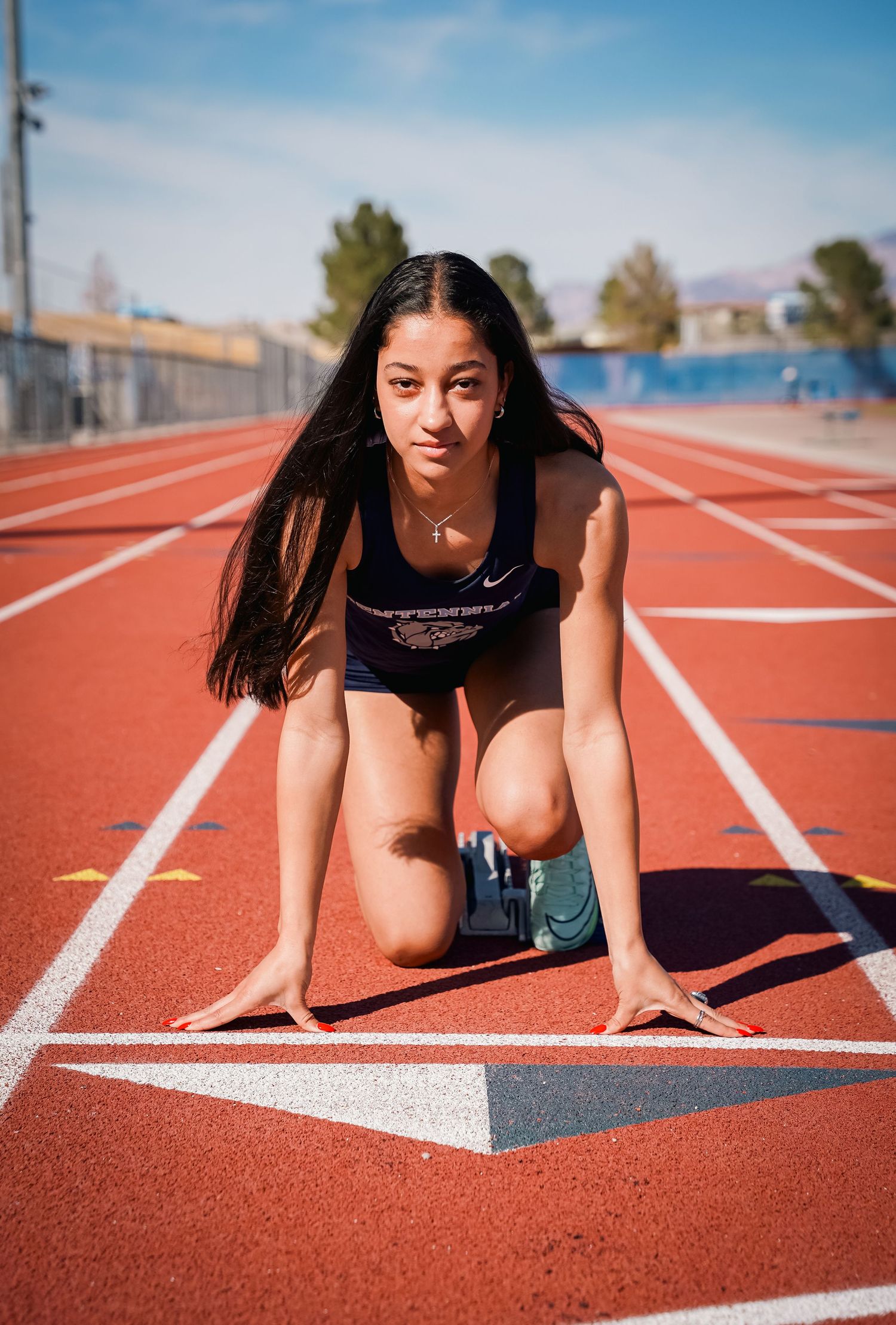 Athlete in starting position on outdoor track with mountains visible in distance.
