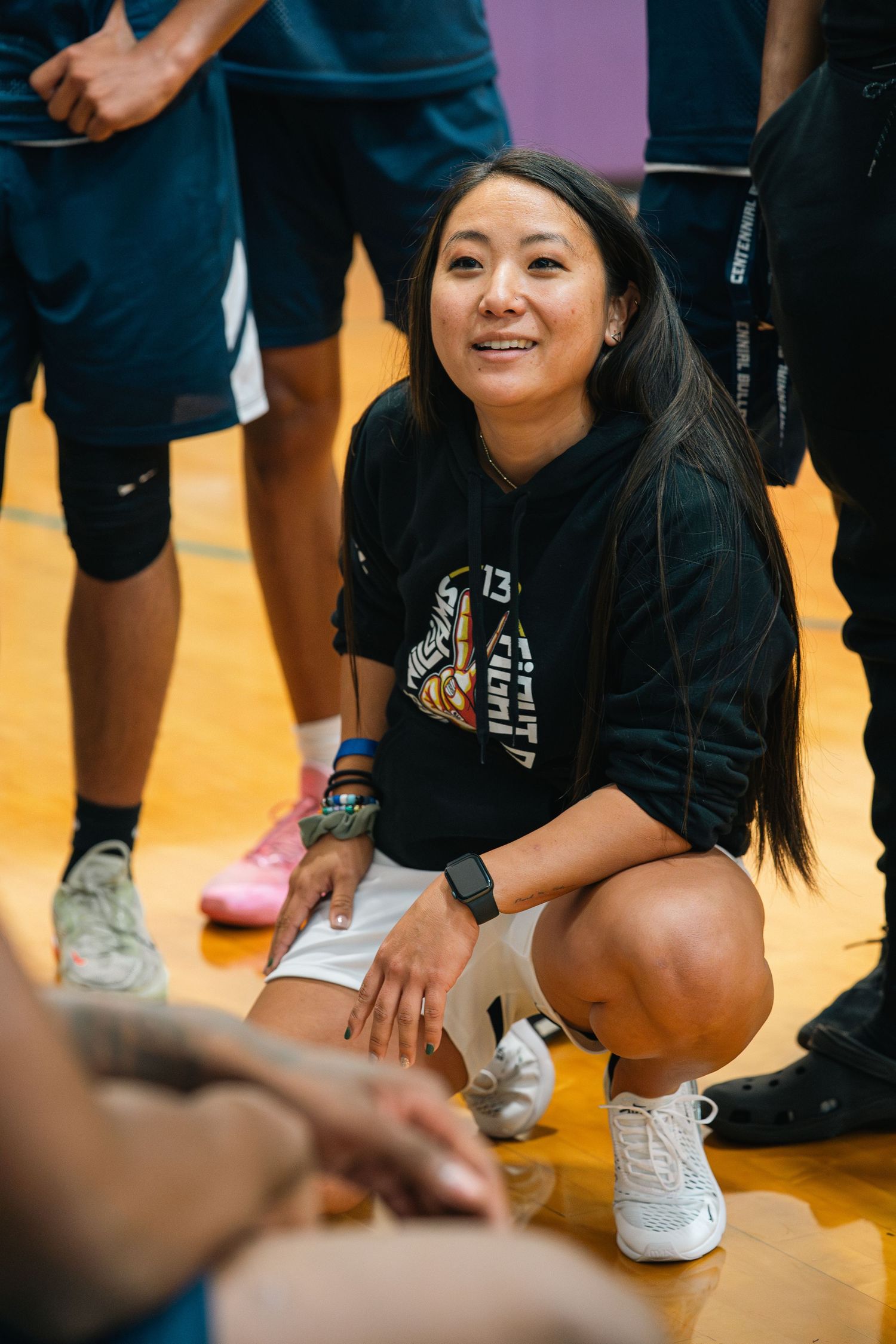 Coach in casual athletic wear crouches down during basketball game.