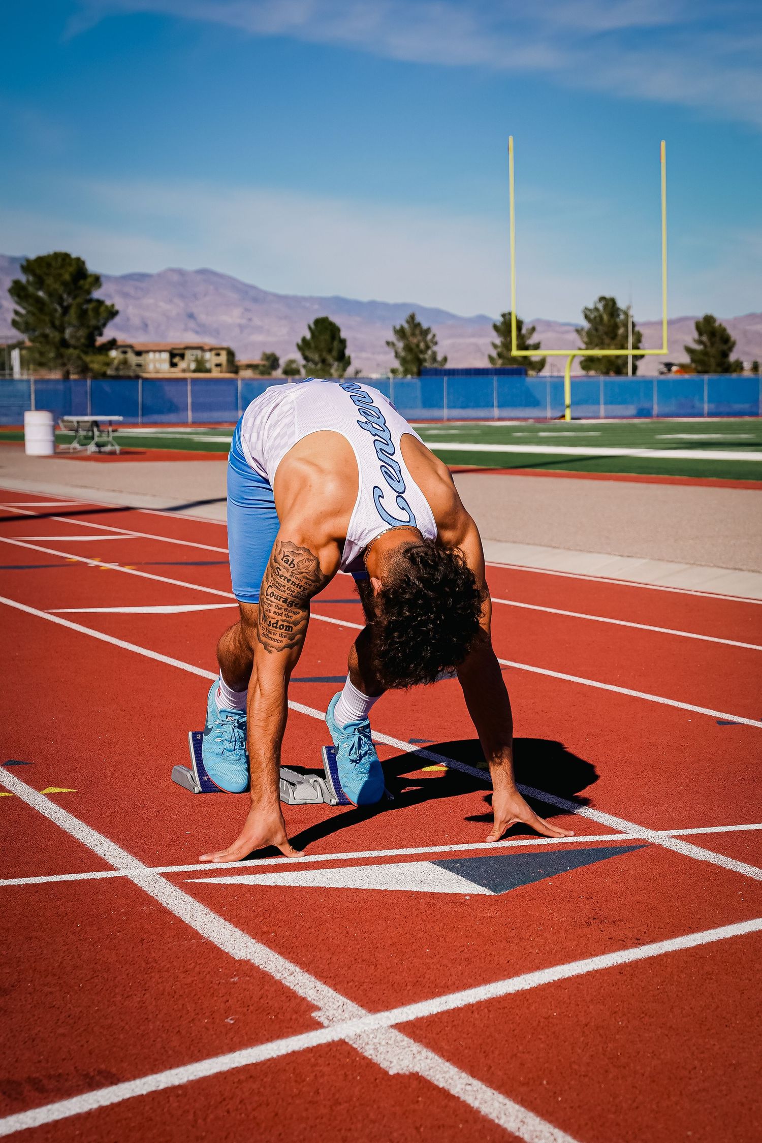 Athletes in starting position on a red running track with mountains in background.