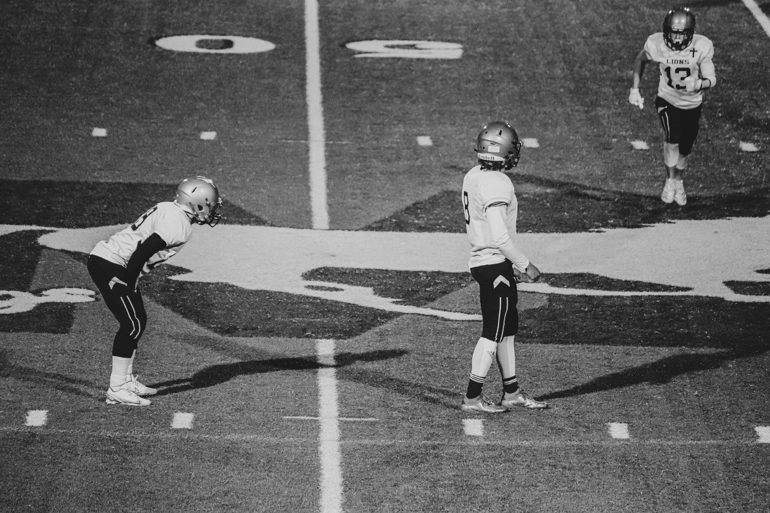 Two football players stretching during practice on field in black and white photography.