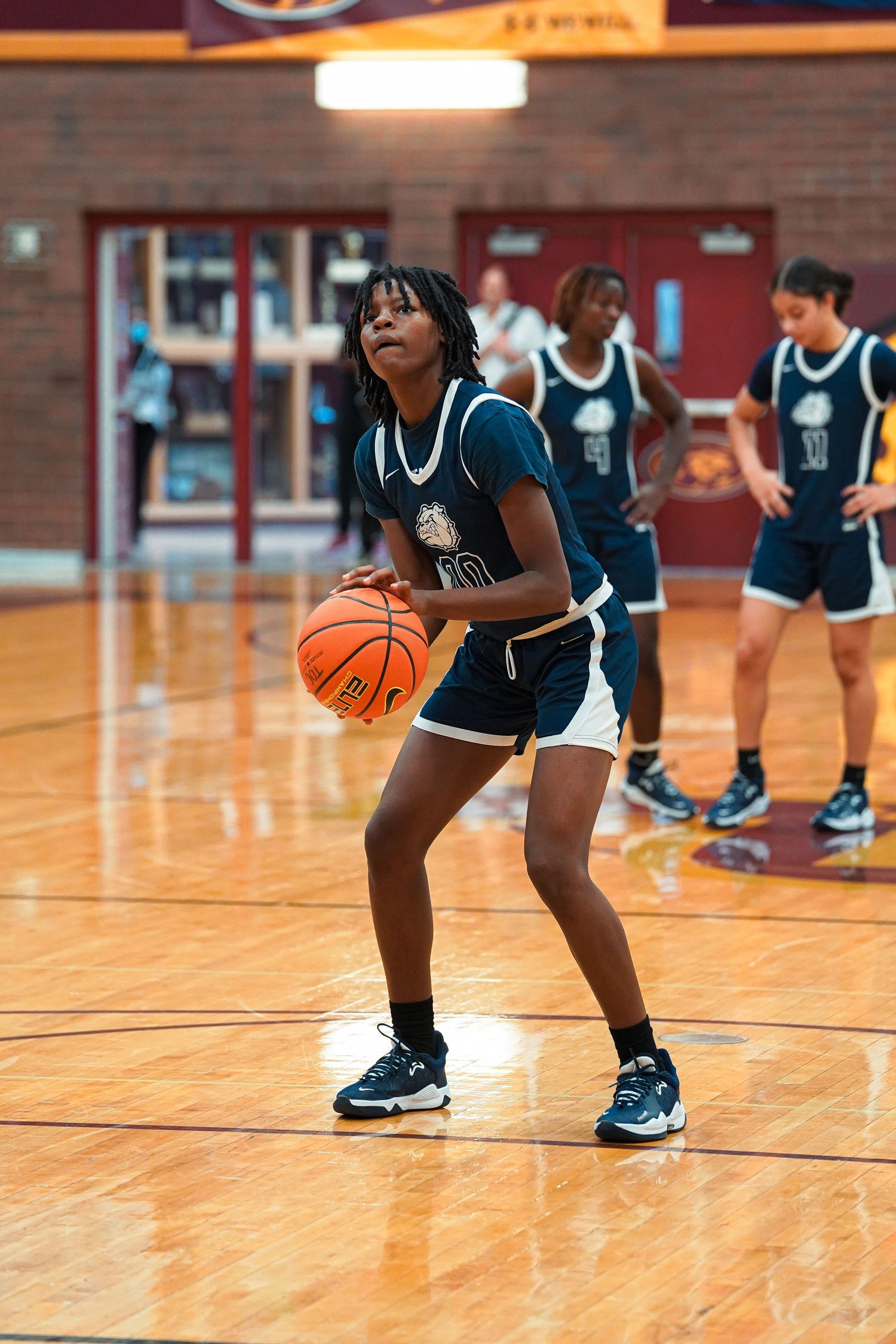 Players in navy uniforms dribbling basketballs during practice drills on gymnasium floor.