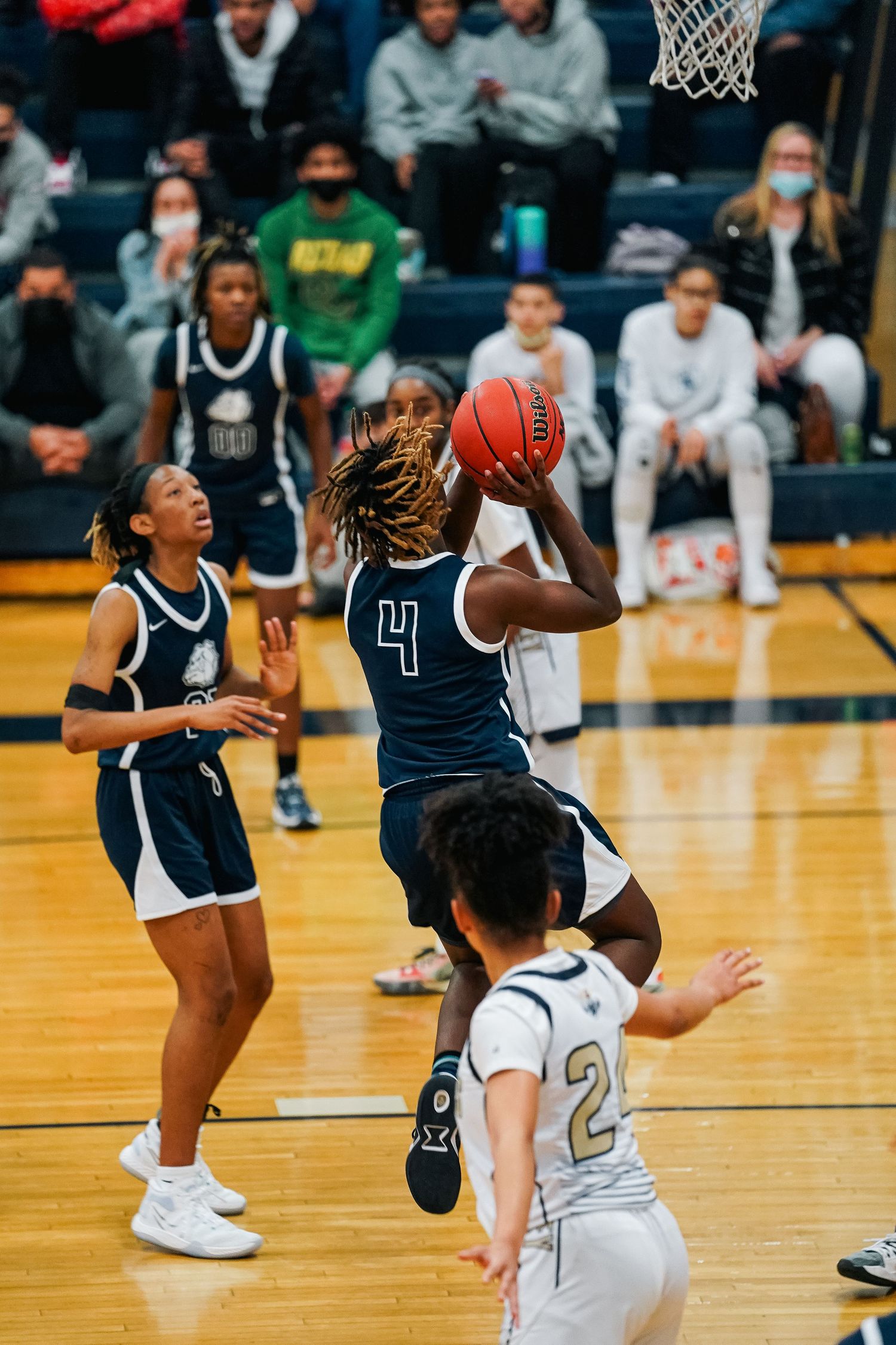 Players in navy and white uniforms face off during an intense basketball game on a wooden court.