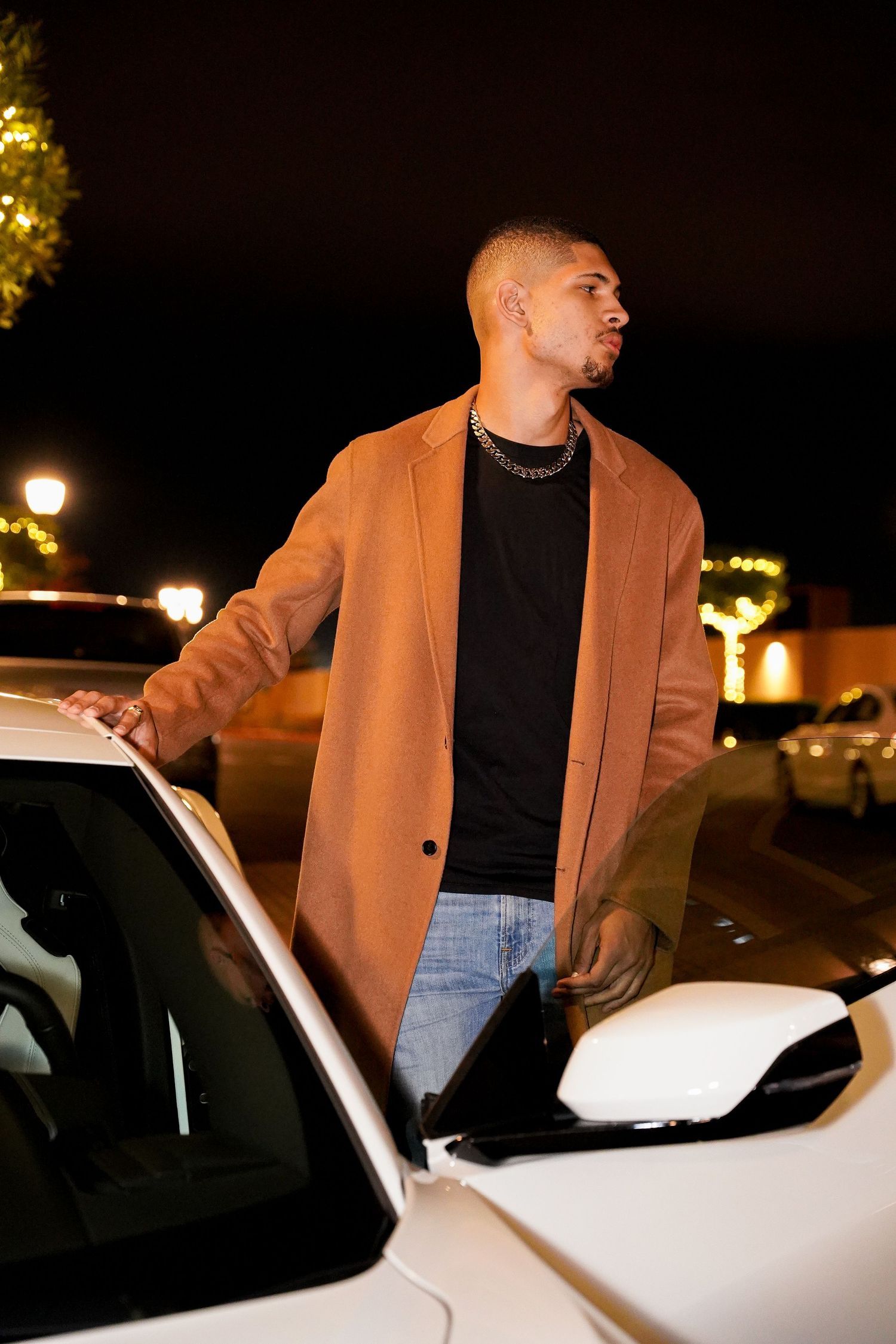 Fashion shots of person in camel coat entering white car under night lighting.