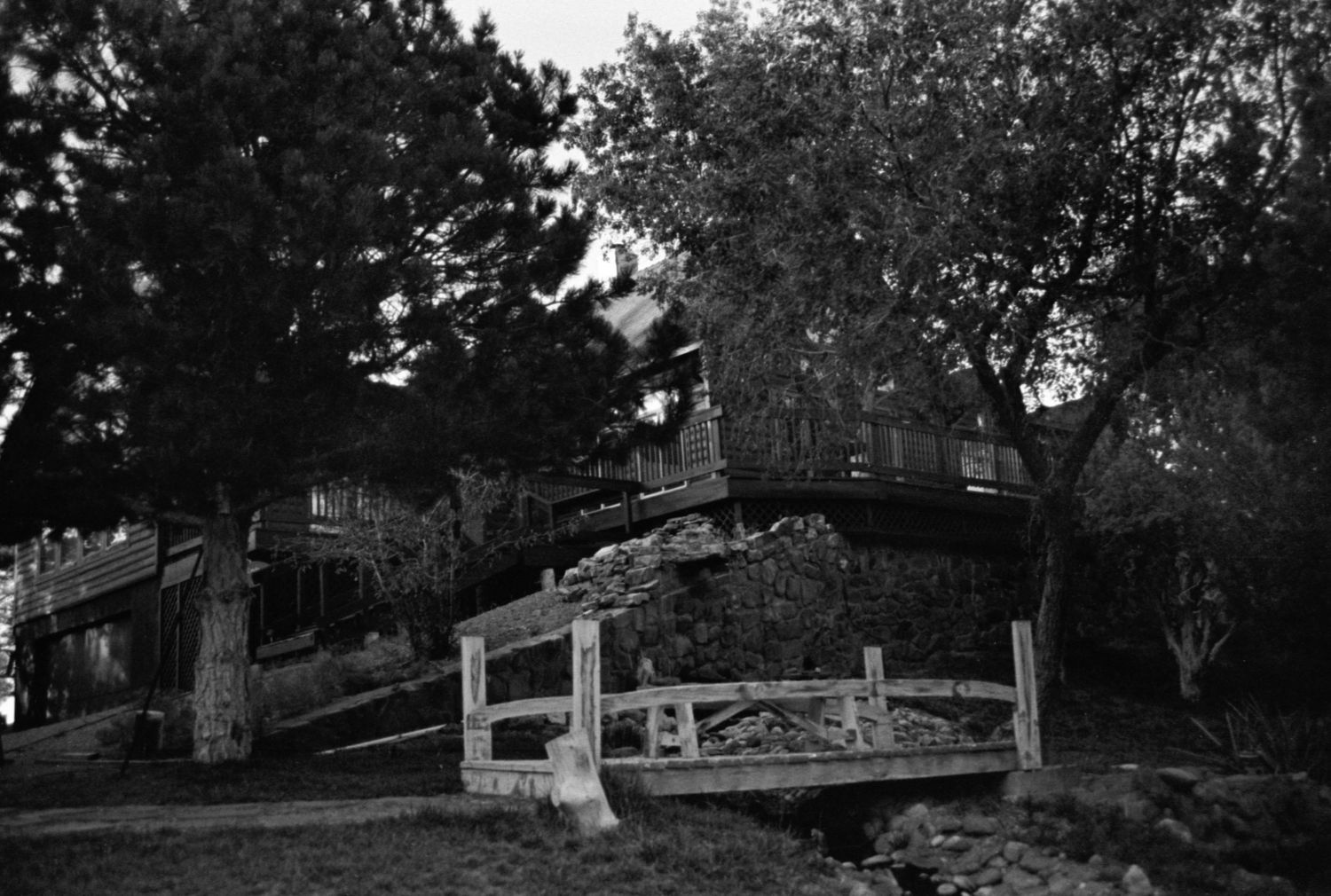 Black and white landscape photograph of trees and wooden fencing at sunset.