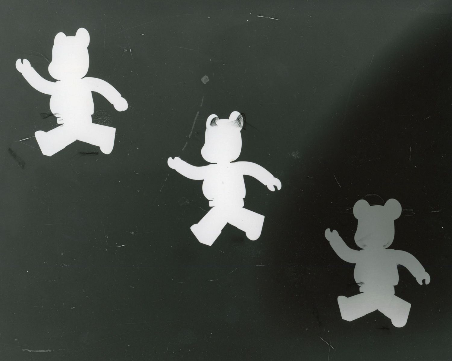 Black and white silhouettes of three teddy bear figures against dark background.