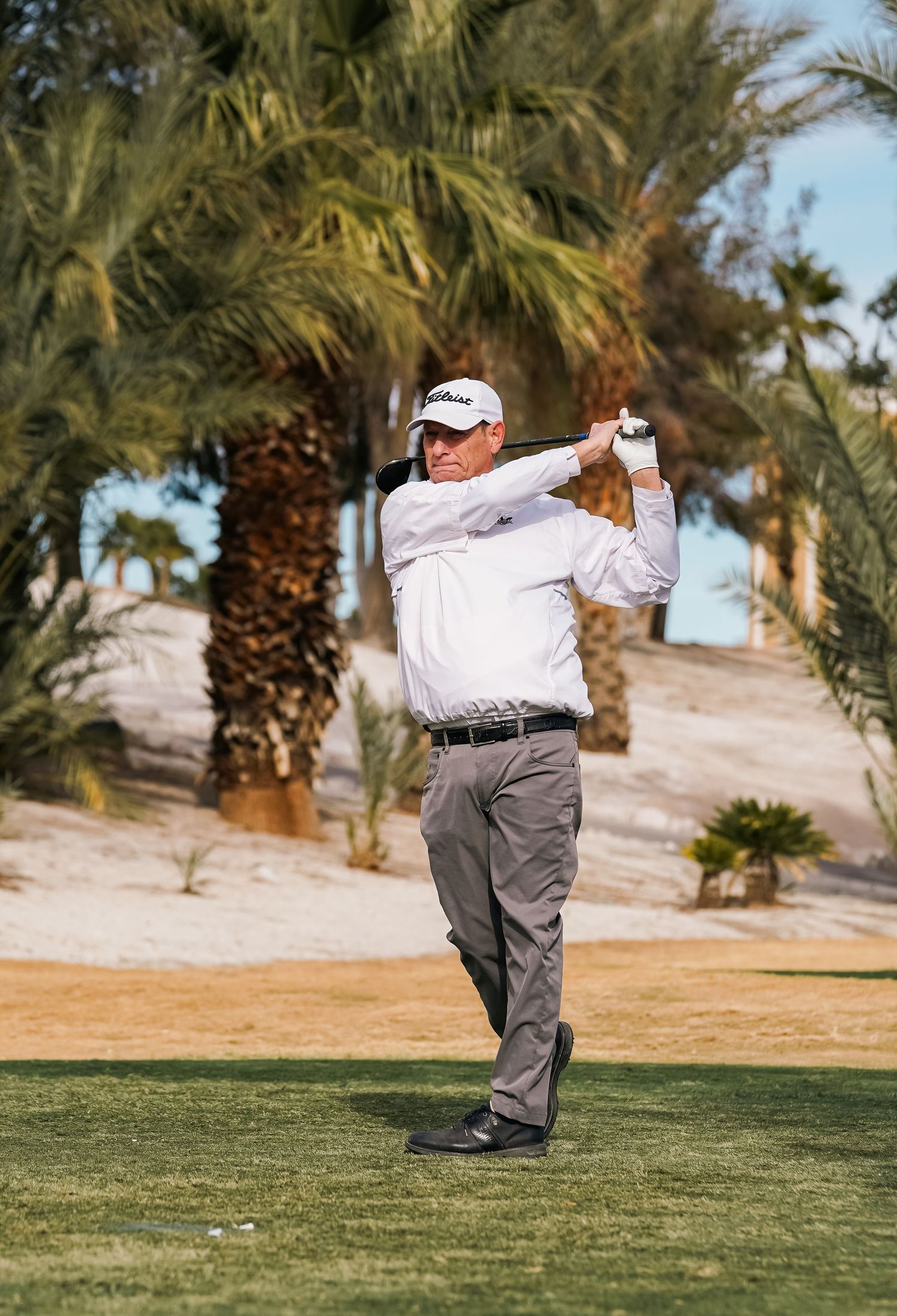 Golfer in white shirt executing a full swing on the desert course.