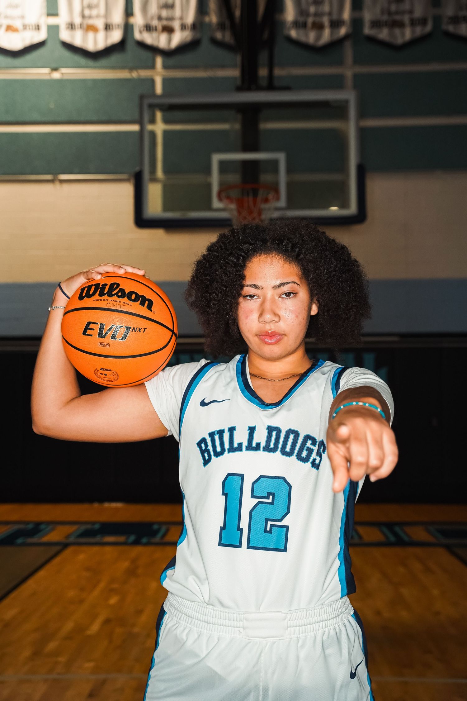Basketball player in white Bulldogs uniform holds basketball while posing in gym.
