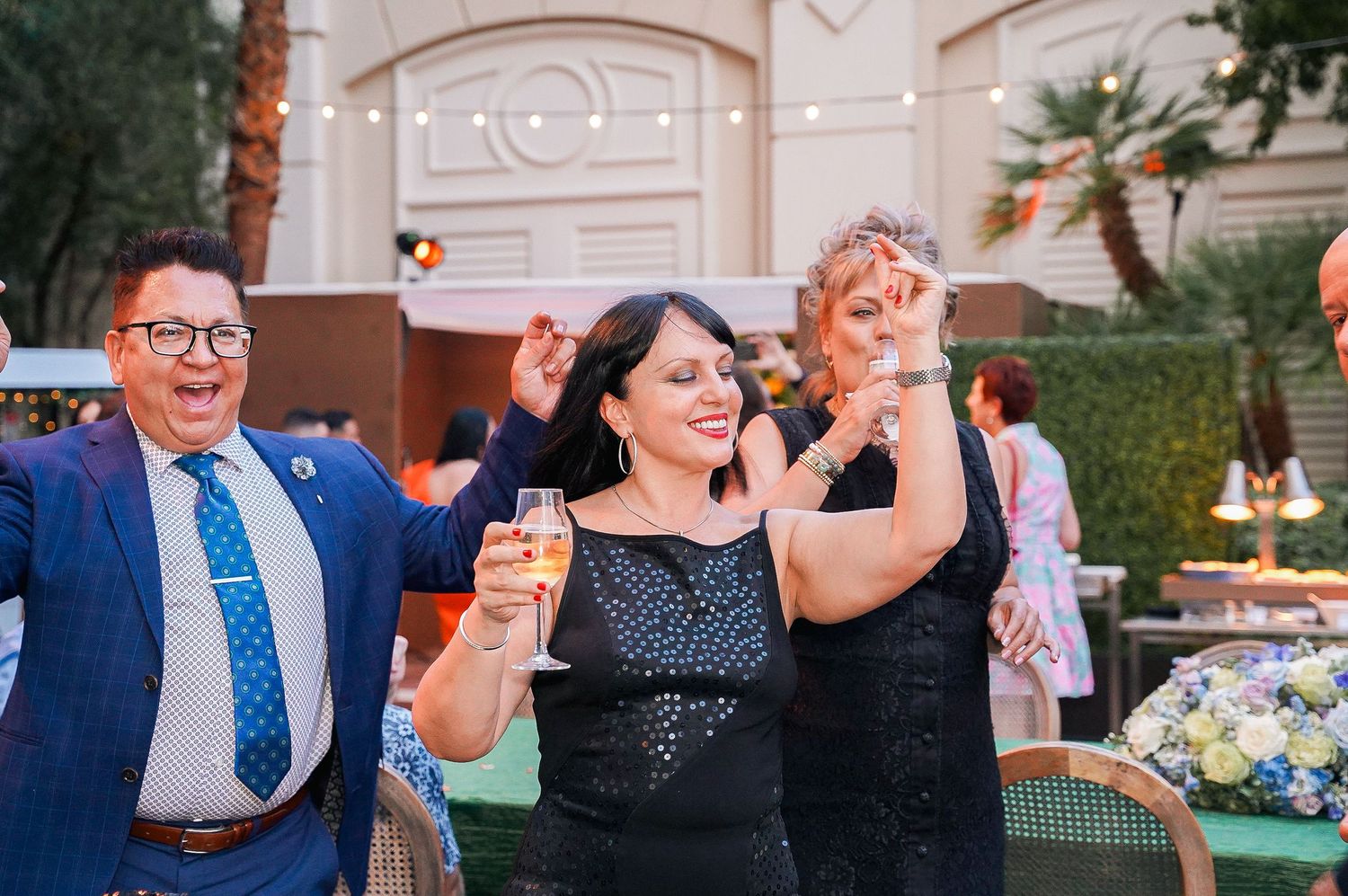 Three party guests celebrating joyfully at an elegant outdoor venue with string lights.