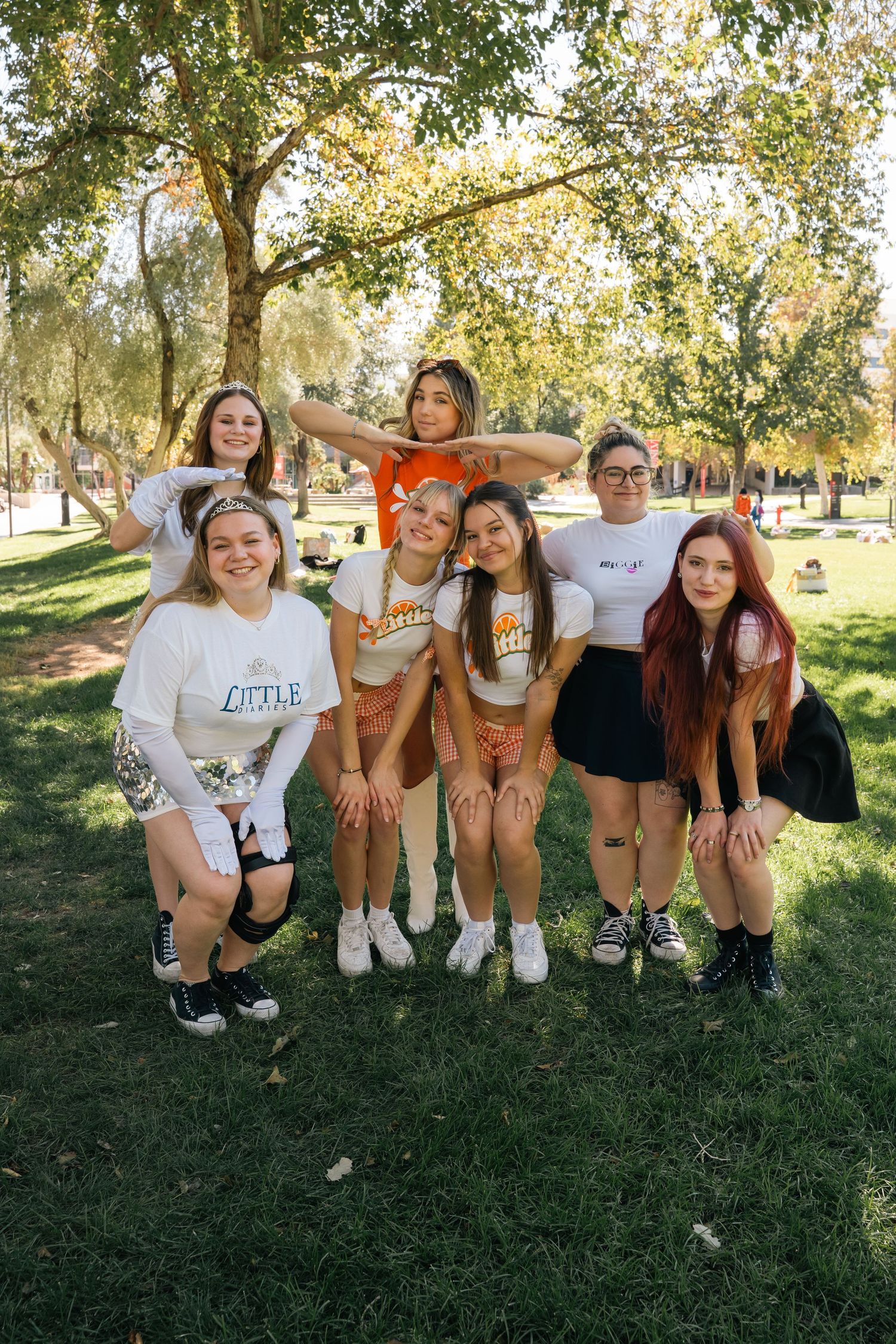 Friends in casual outfits strike playful poses together on sunny campus lawn.