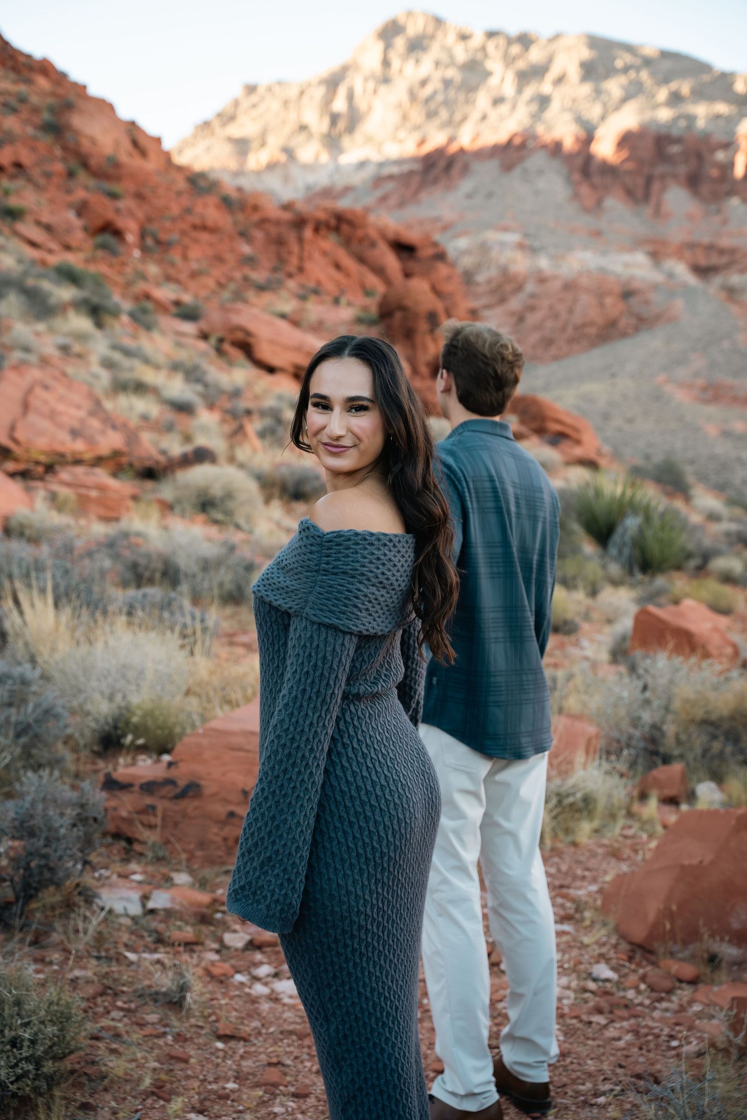 A couple in coordinated outfits posing against stunning red rock formations.