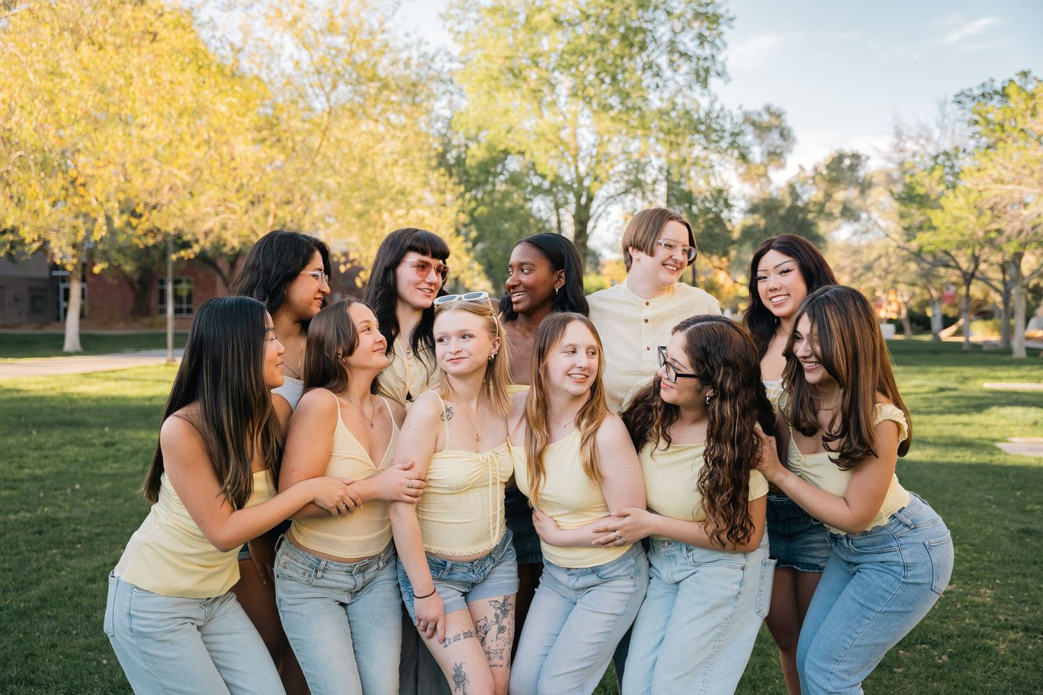 Friends gather for a candid group photo wearing coordinated pastel tops and denim on a sunny day.