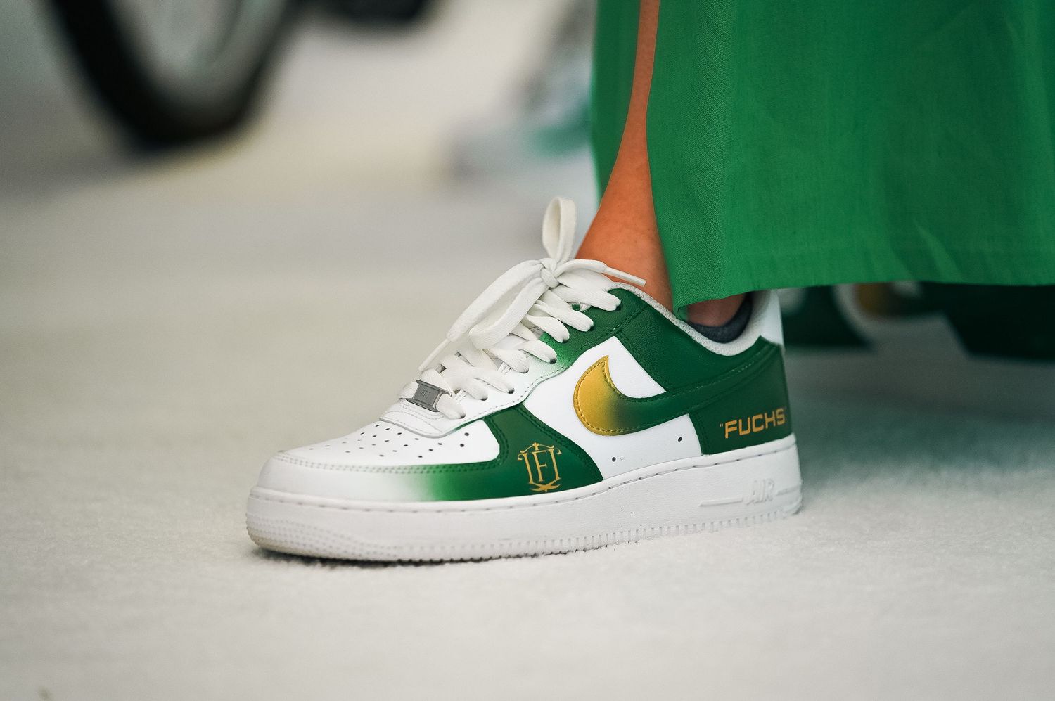 Close-up of white and green Nike Air Force 1 sneaker with gold accents.