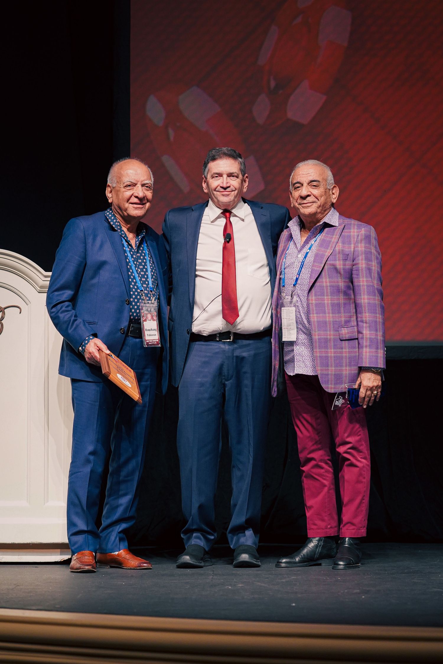 Three men in suits standing together on stage during a Vegas presentation.