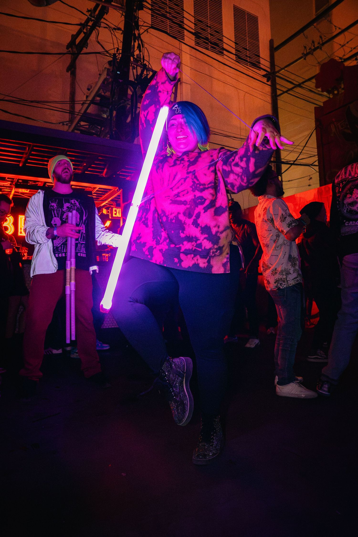 Person holding glowing purple light stick at nightclub with neon lighting.