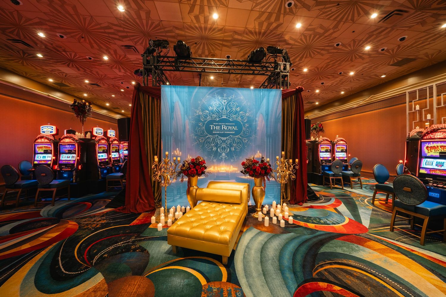 Elegant casino gaming area featuring slot machines and a theatrical stage with dramatic lighting and patterned carpeting.