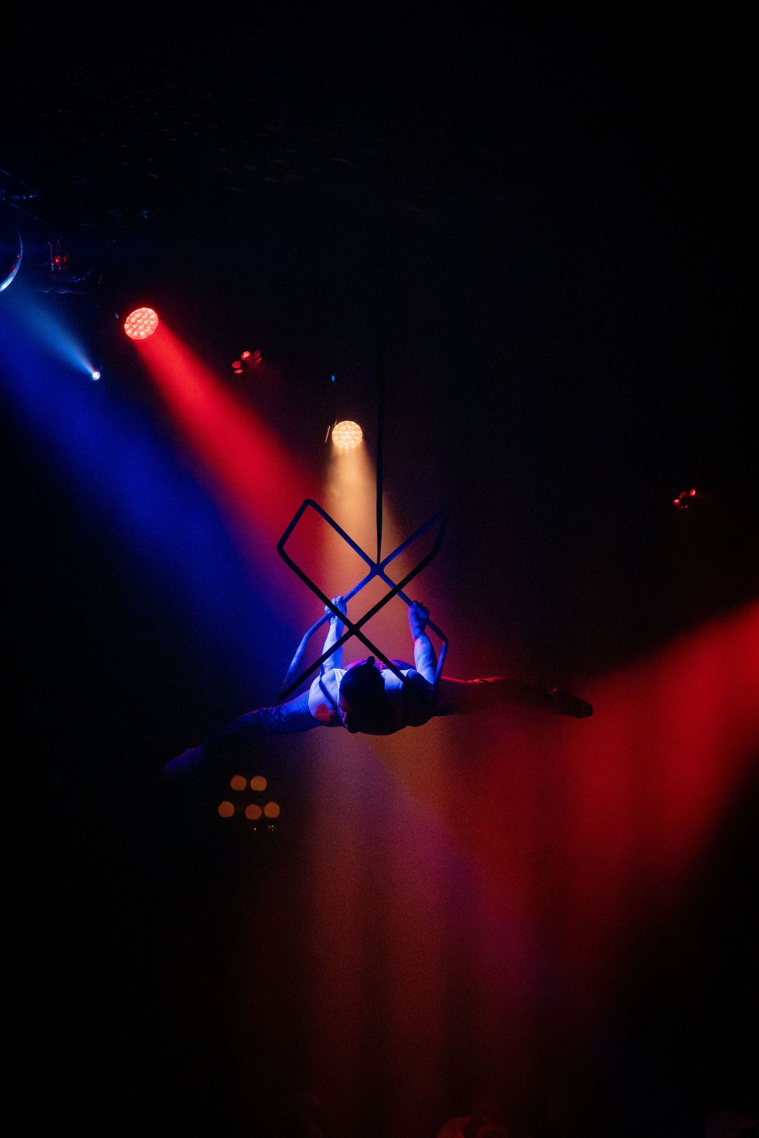 Aerial performer silhouetted against dramatic blue and red stage lighting.
