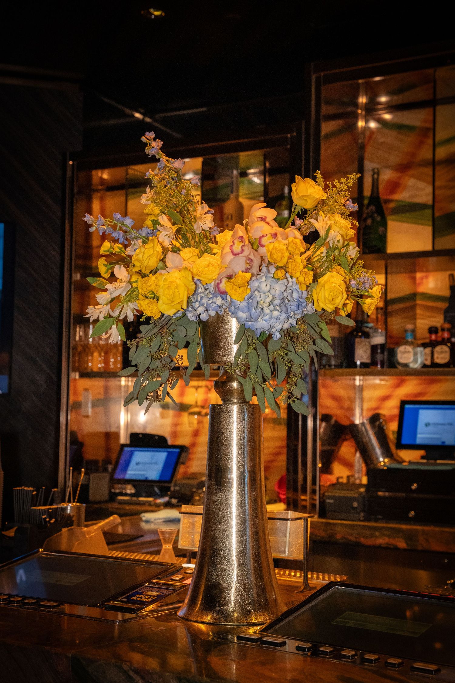 Elegant floral arrangement with yellow roses and blue hydrangeas on a bar counter.