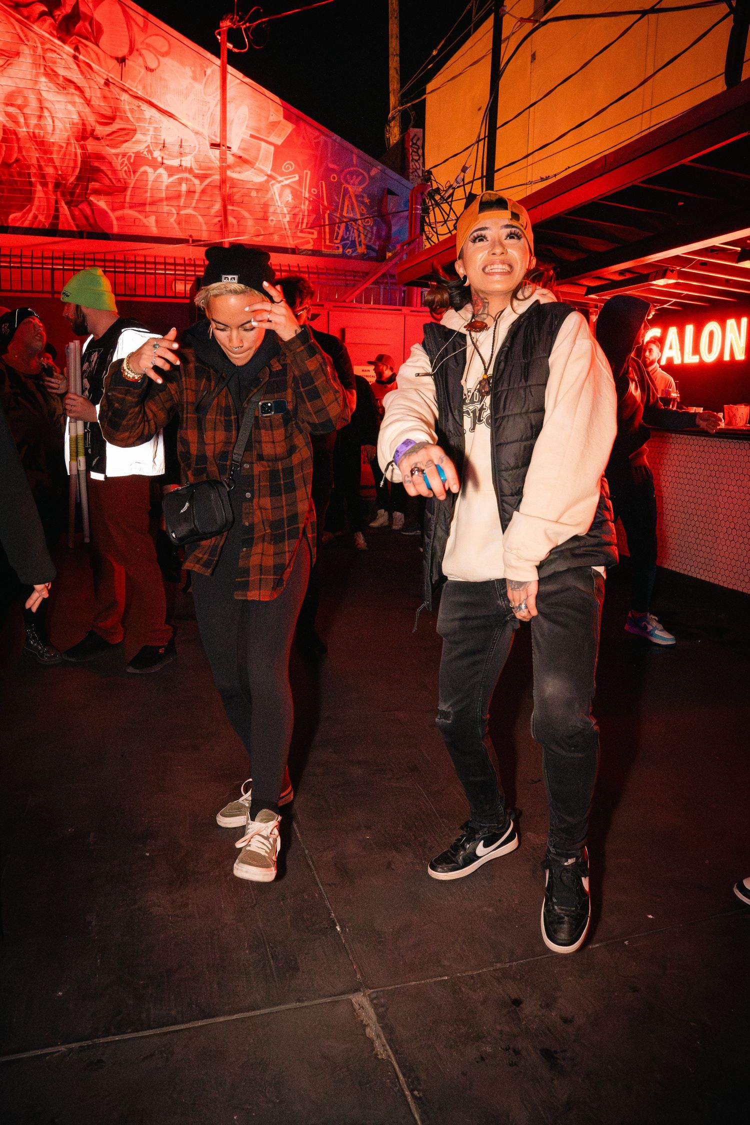 Two people dancing and gesturing under red lighting in an urban nightclub setting.