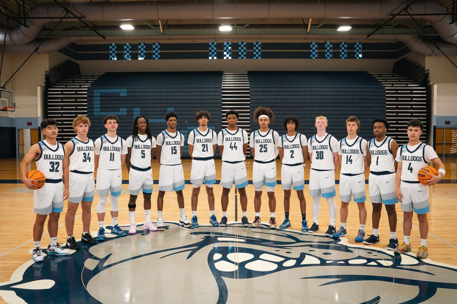 Basketball team in white jerseys stands on court with school logo for official team photo.