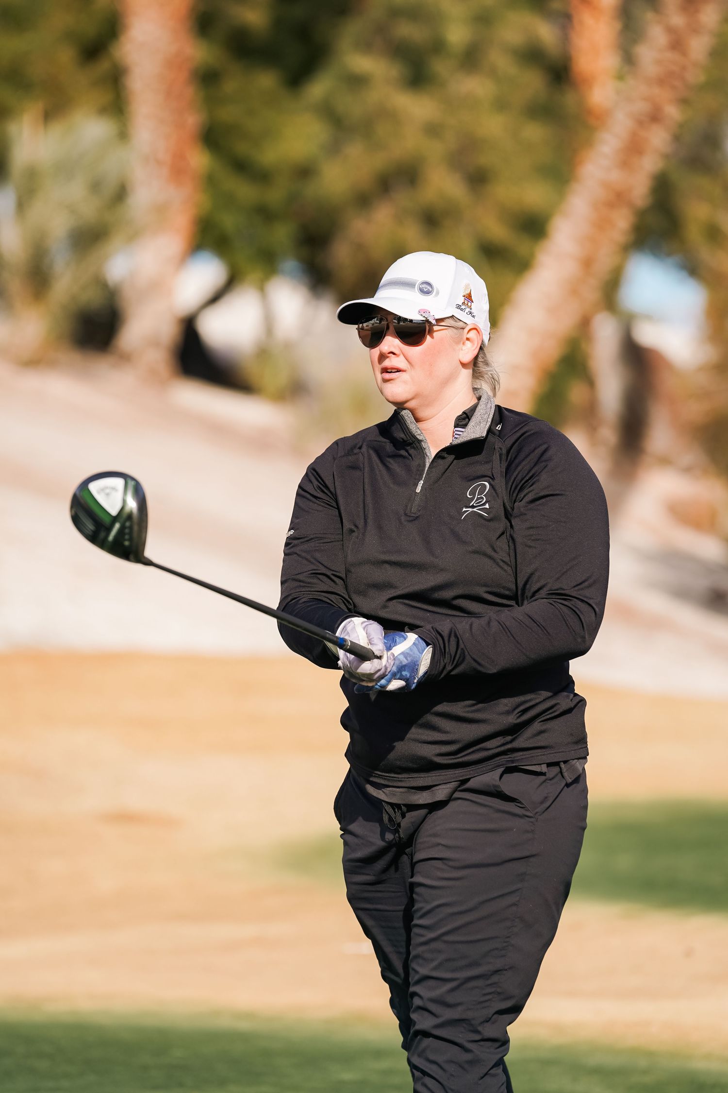 Golfer in black attire taking a swing with a driver on a sunny golf course.