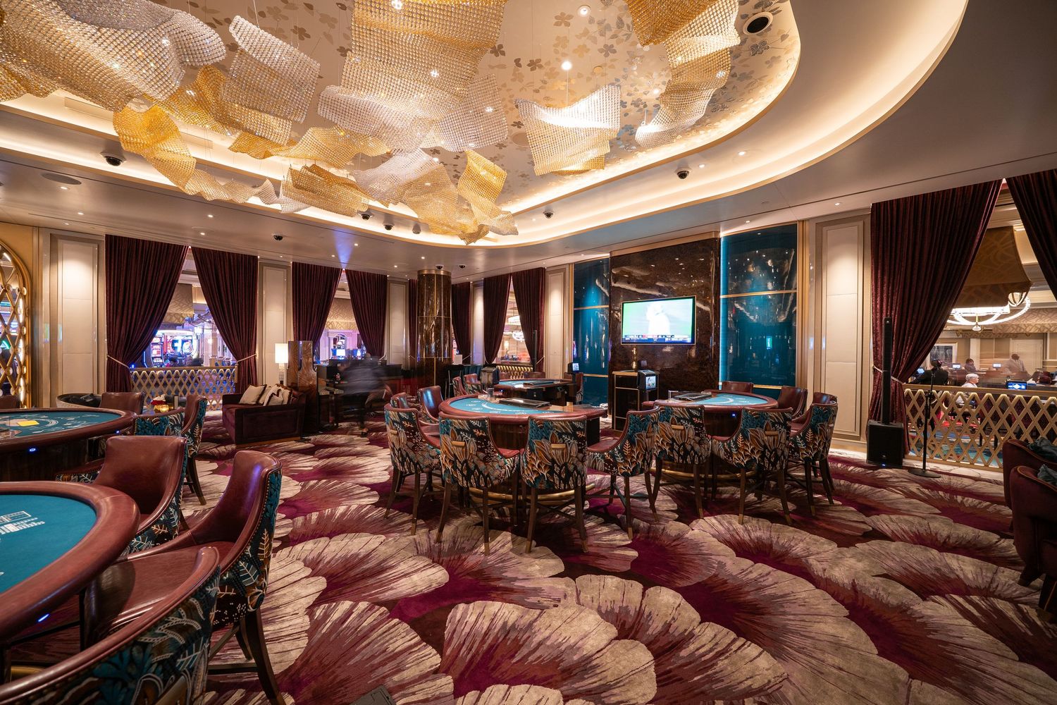 Opulent casino gaming room with golden ceiling details and burgundy patterned carpet.