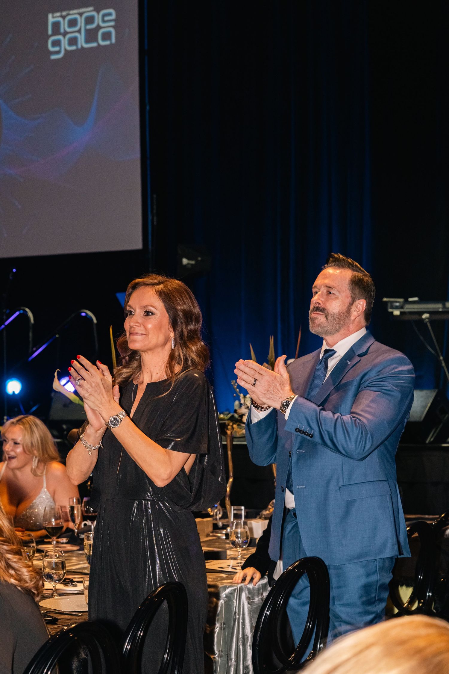 Two people in formal attire applauding during an event with Hope Gala branding.