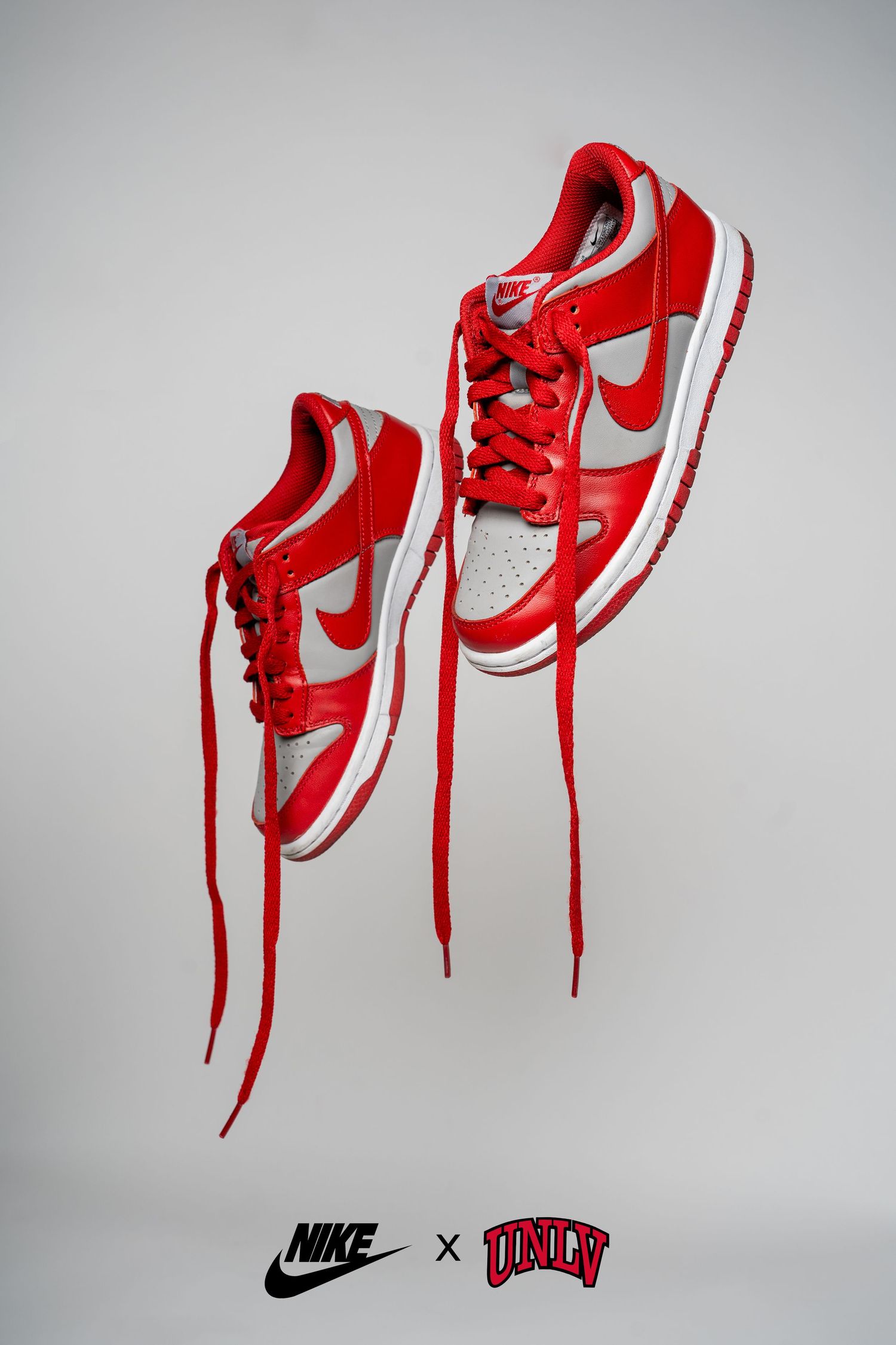 Suspended red and white Nike sneakers with long laces against a grey background.