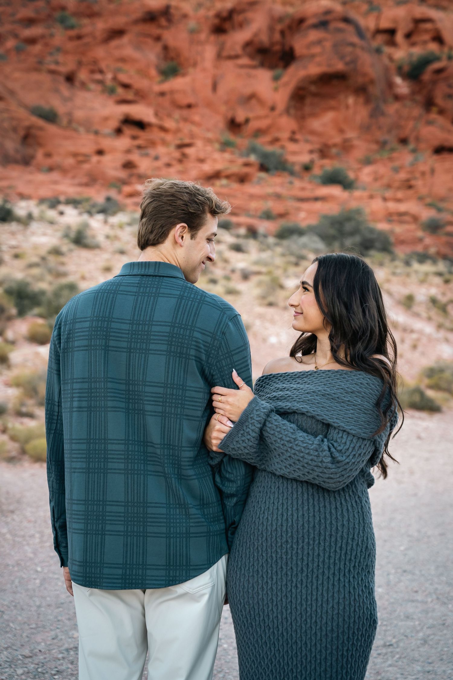 Couple walking together in cozy sweaters along desert trail.