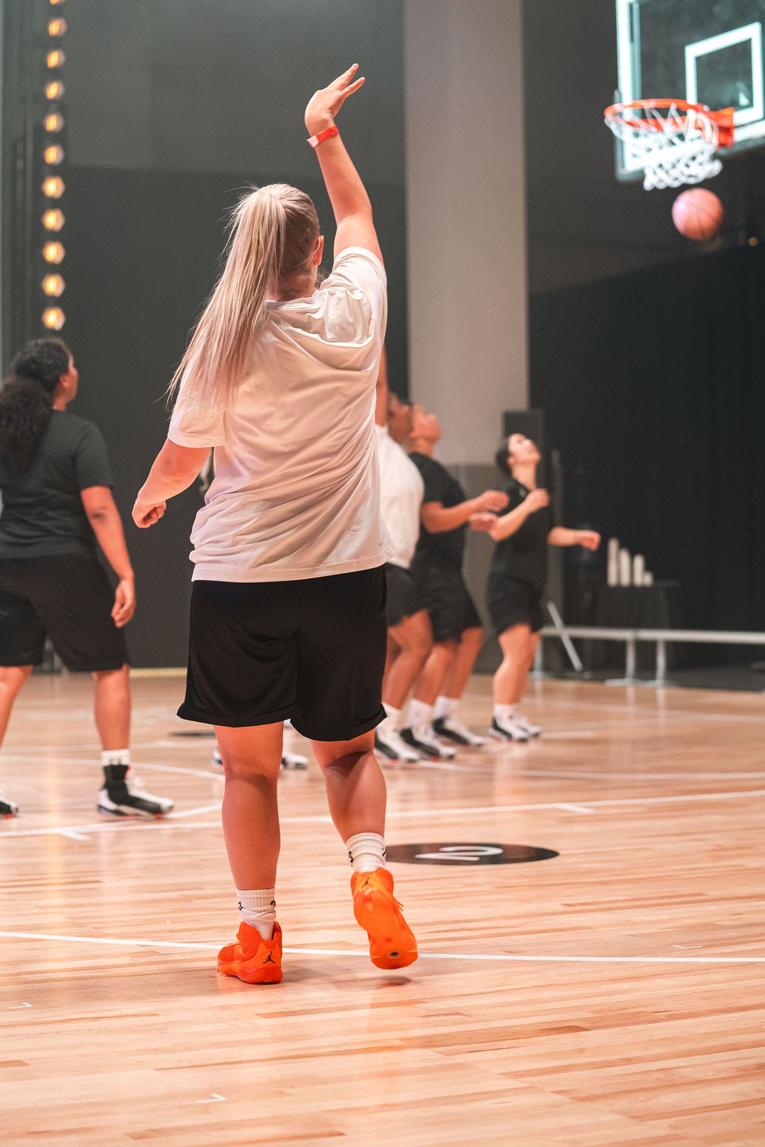 Player in white shirt and black shorts practicing basketball on indoor wooden court.