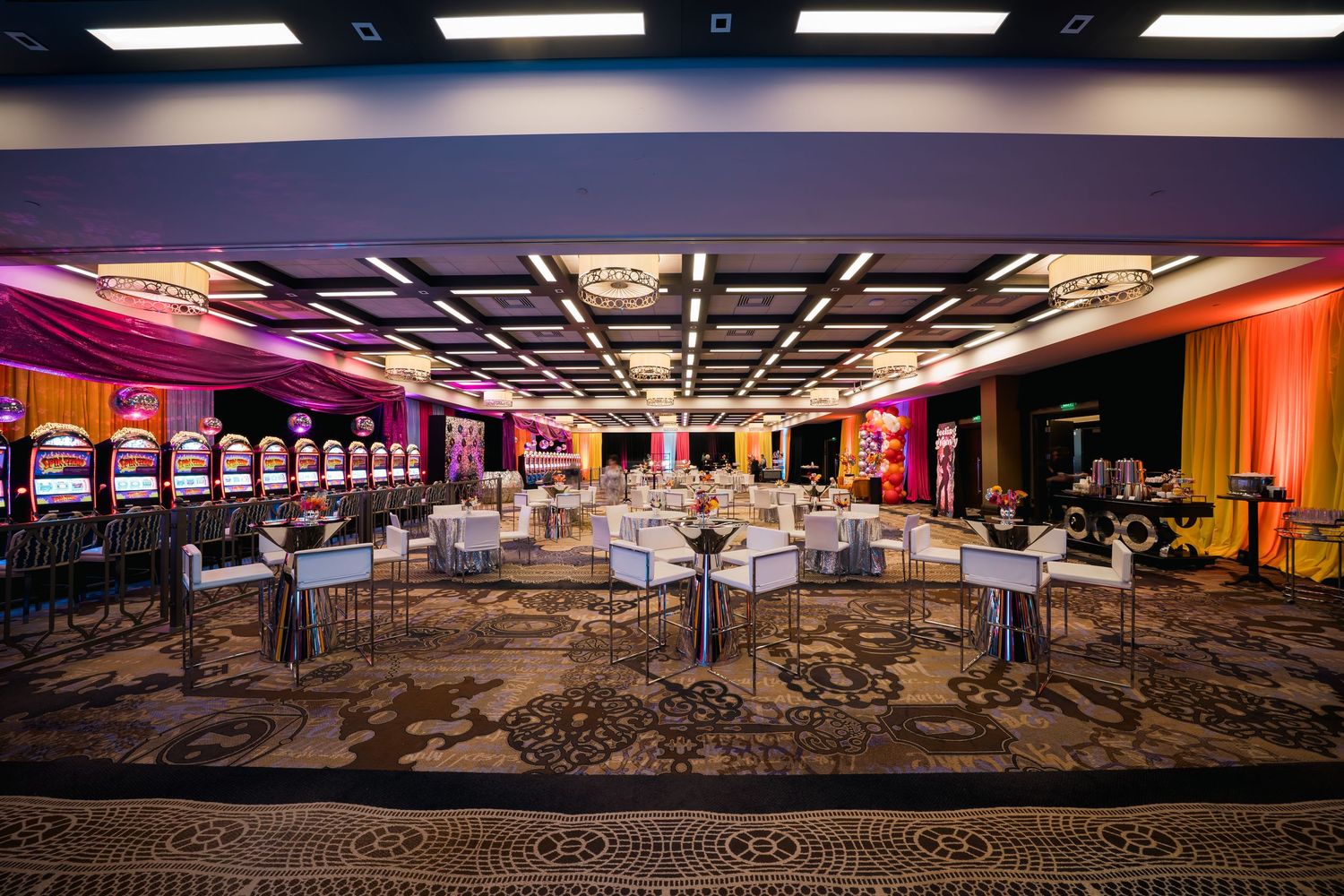 Modern casino ballroom with geometric ceiling design and colorful mood lighting.