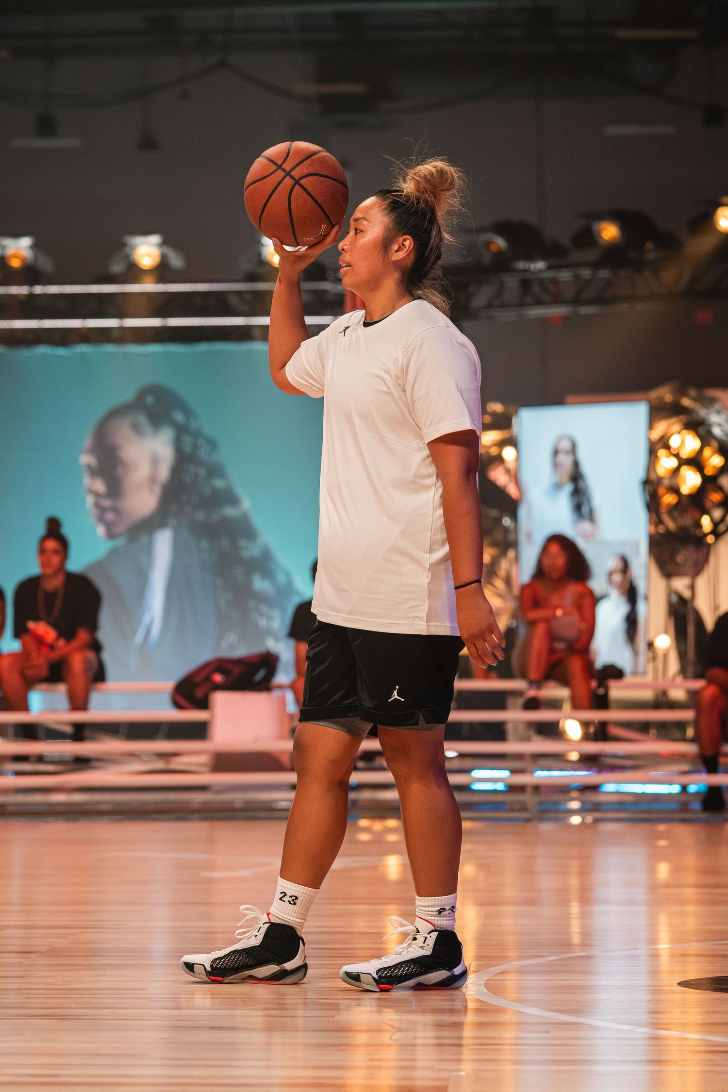 Athletes practicing basketball drills on an indoor wooden court with projection screen.