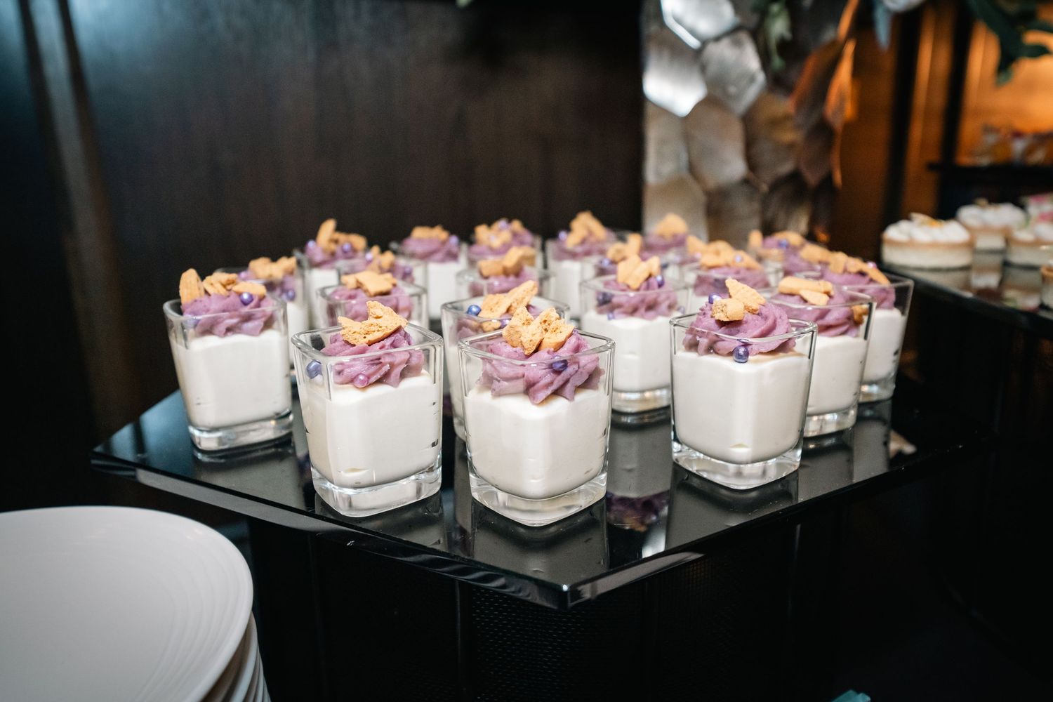 Small glass dessert cups filled with creamy mousse and topped with purple flowers on a dark display.