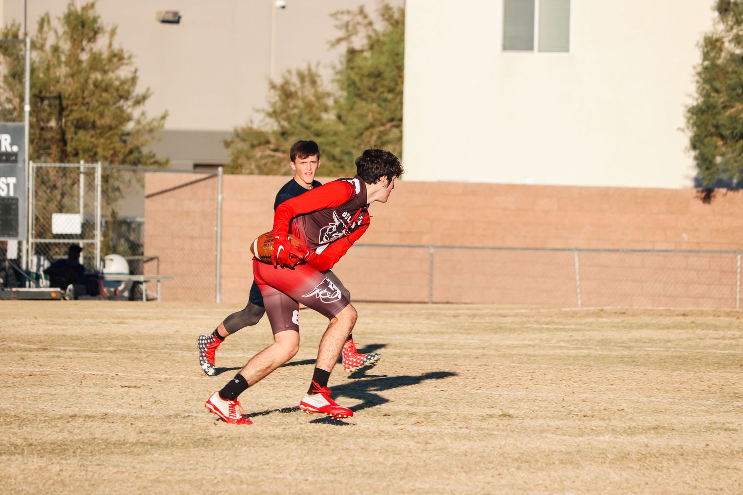 Athletes in red jerseys run across a dry grass field during a sports practice session.