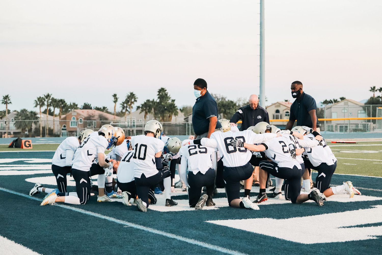 Football players sitting in formation on white sideline markings.