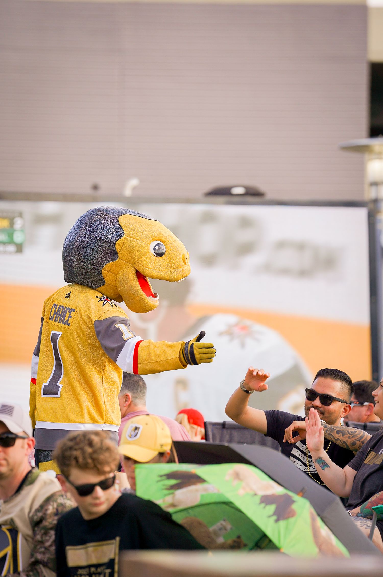 Vegas Golden Knights mascot Chance the yellow dinosaur interacts with fans at outdoor event.