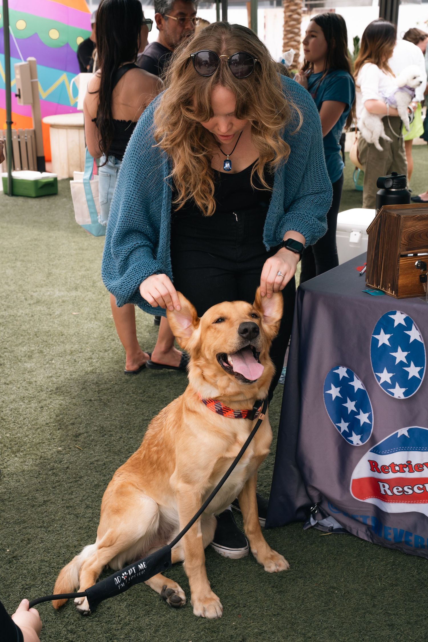 Woman petting happy golden retriever at outdoor pet adoption event with patriotic themed display.