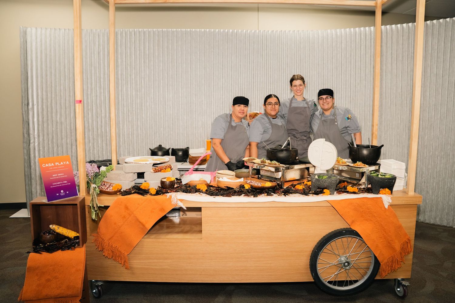 Food service staff pose behind wooden cart display of catering items.