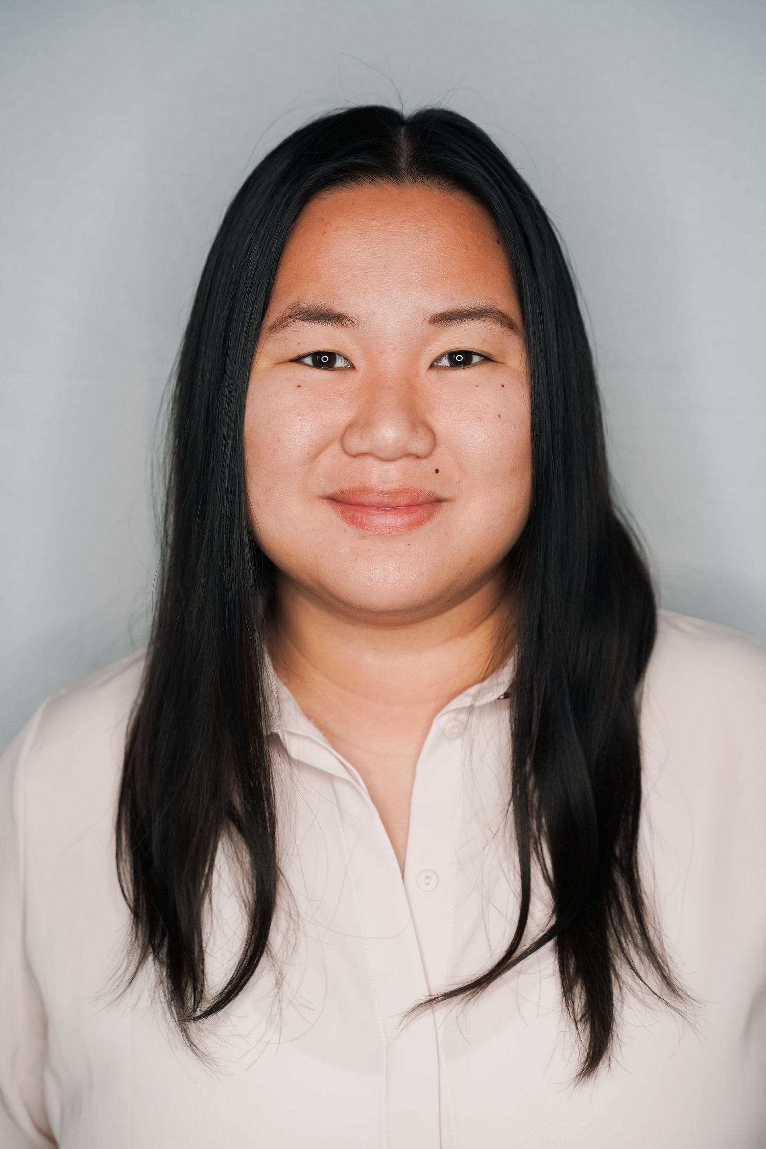 Monaco Media. Portrait of person with long black hair in cream blouse smiling against neutral backdrop.